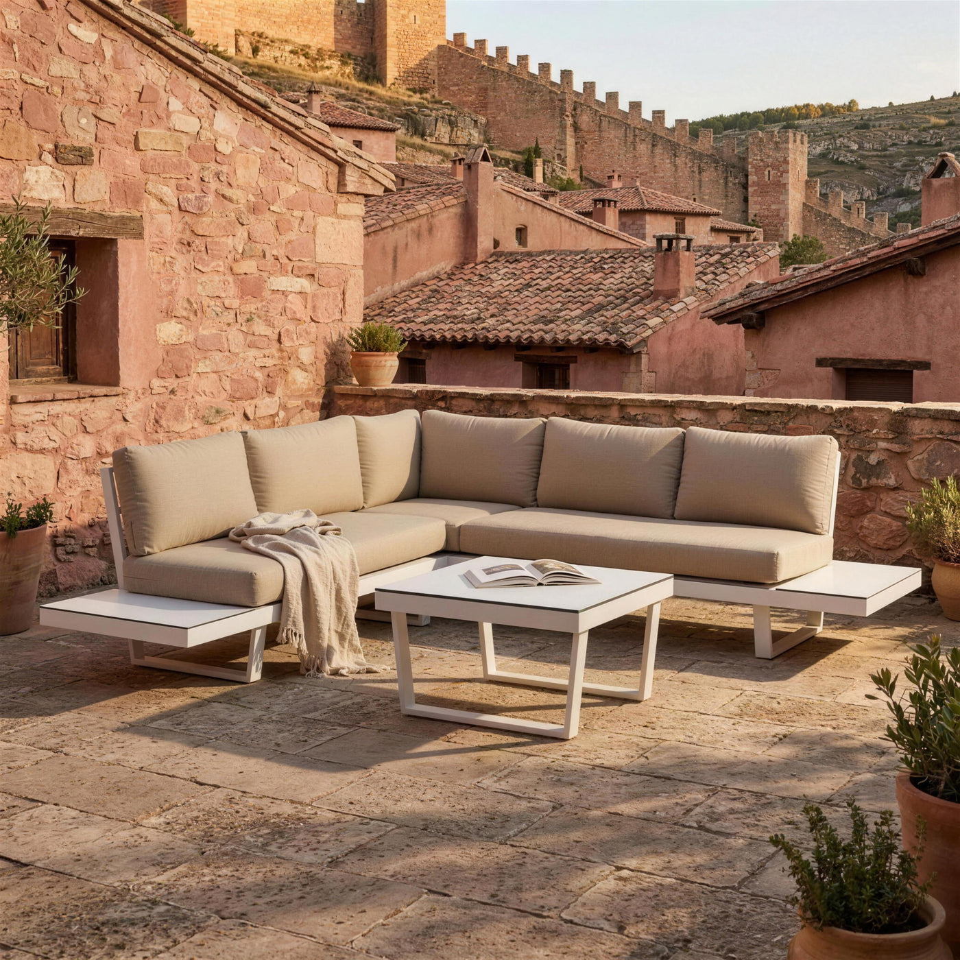 Rinconera Loira-7 en una terraza empedrada de Albarracin, Teruel, con muros de rodeno rosado, tejados de teja y la muralla en la ladera, con una manta de lino y un libro abierto