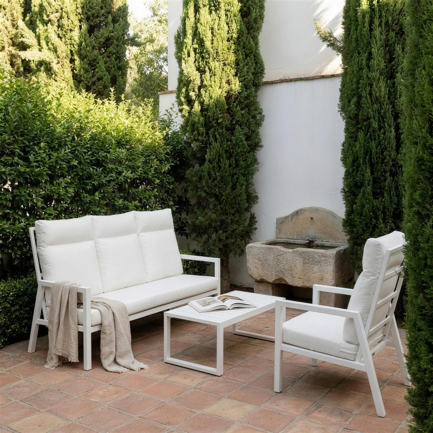Conjunto Haston blanco en el jardin de un carmen del Albaicin granadino, entre cipreses y un pilon de piedra, con una manta de lino sobre el sofa