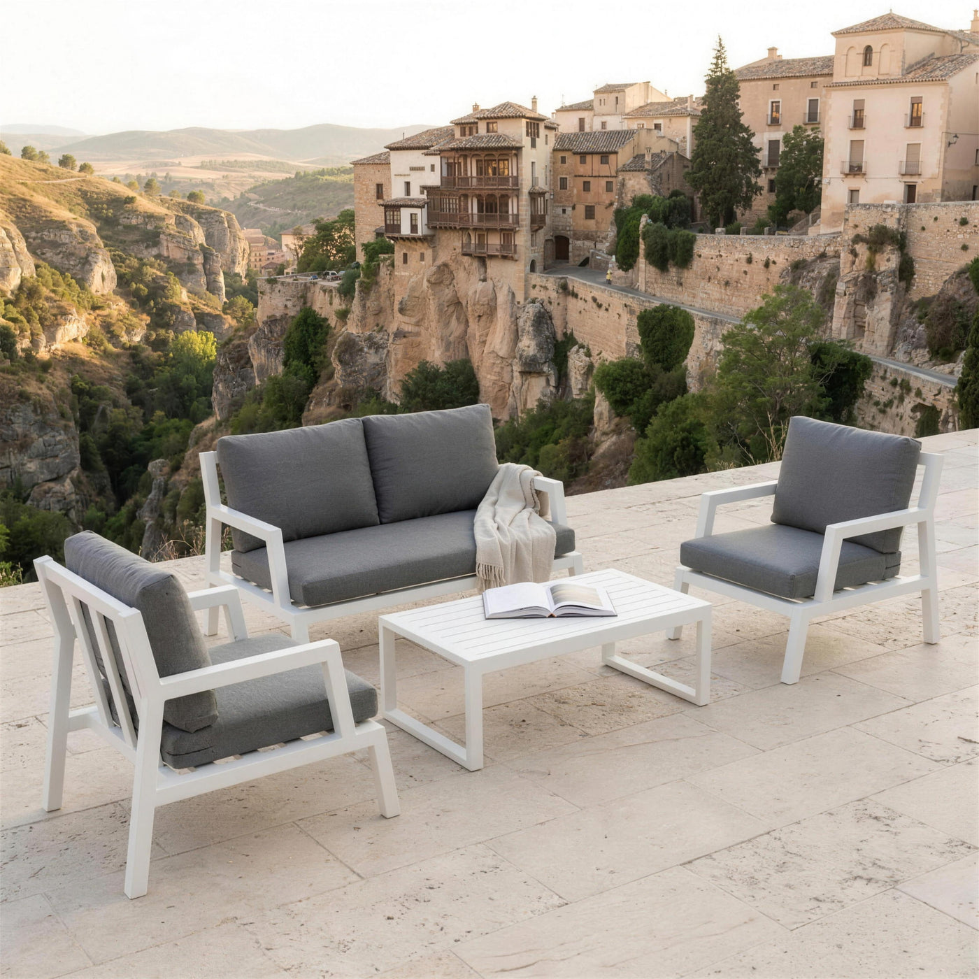 Conjunto Leisa blanco en una terraza de caliza sobre la hoz del Huecar, con las casas colgadas de Cuenca al fondo, manta de lino y un libro abierto