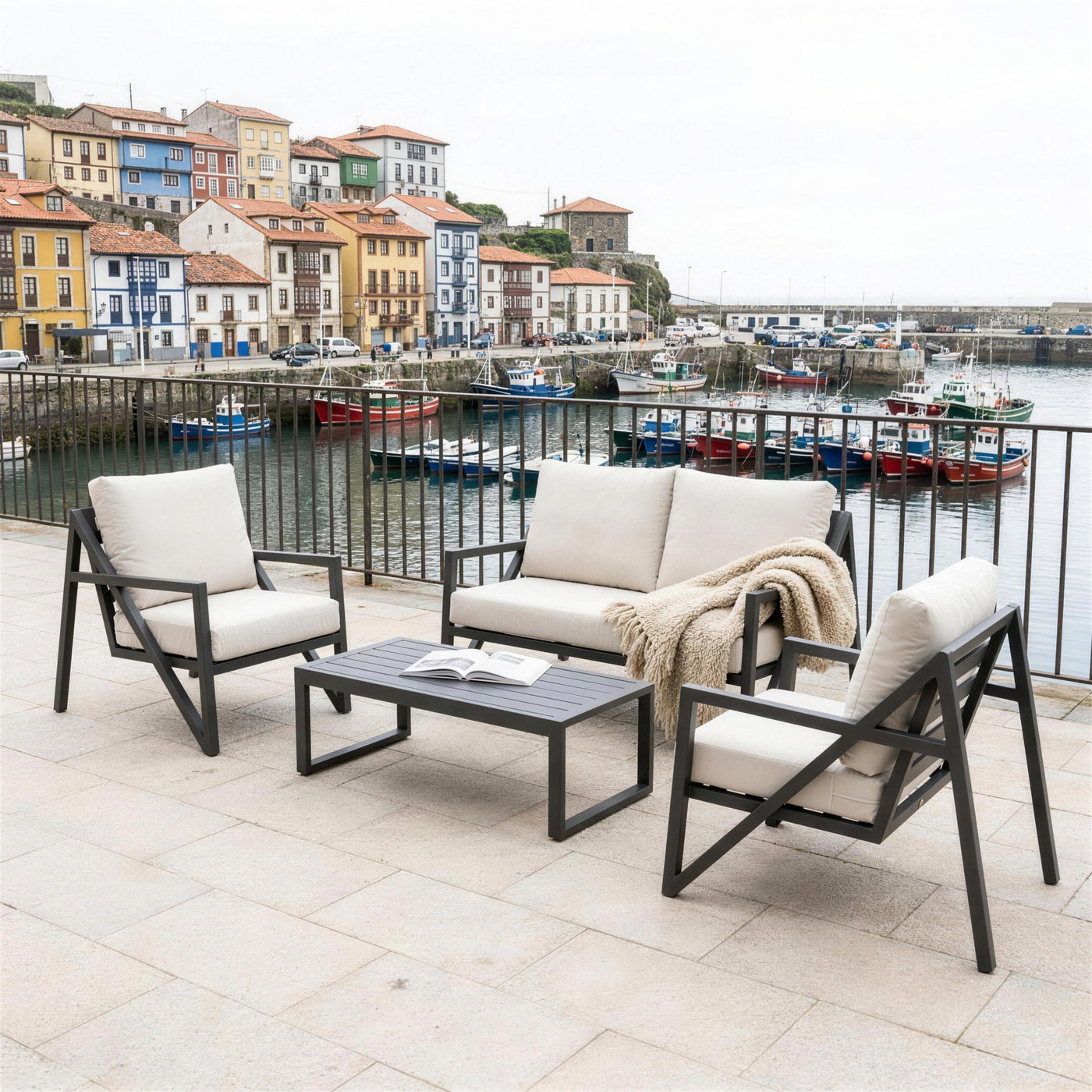 Set de jardín antracita en una terraza asturiana sobre el puerto pesquero, con las casas del pueblo y las barcas al fondo