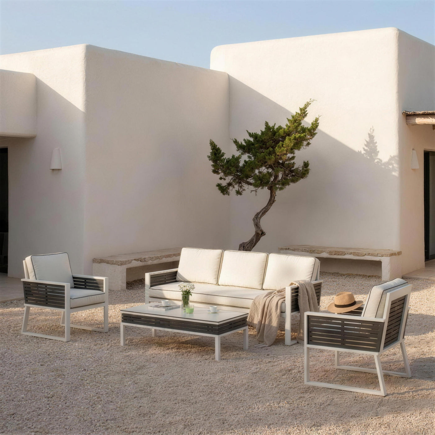 Set de jardín bicolor en el patio encalado de una casa payesa de Ibiza, con sabina y suelo de grava clara