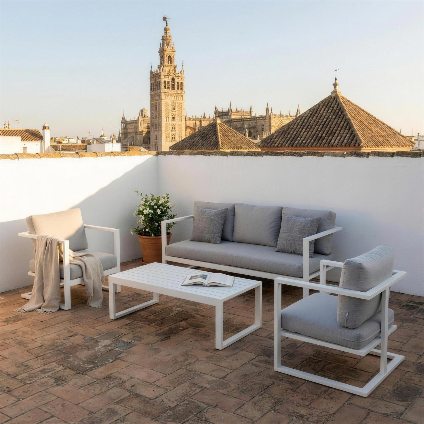 Set de jardín blanco en una azotea sevillana de suelo de ladrillo, con jazmín en tinaja y la Giralda sobre los tejados