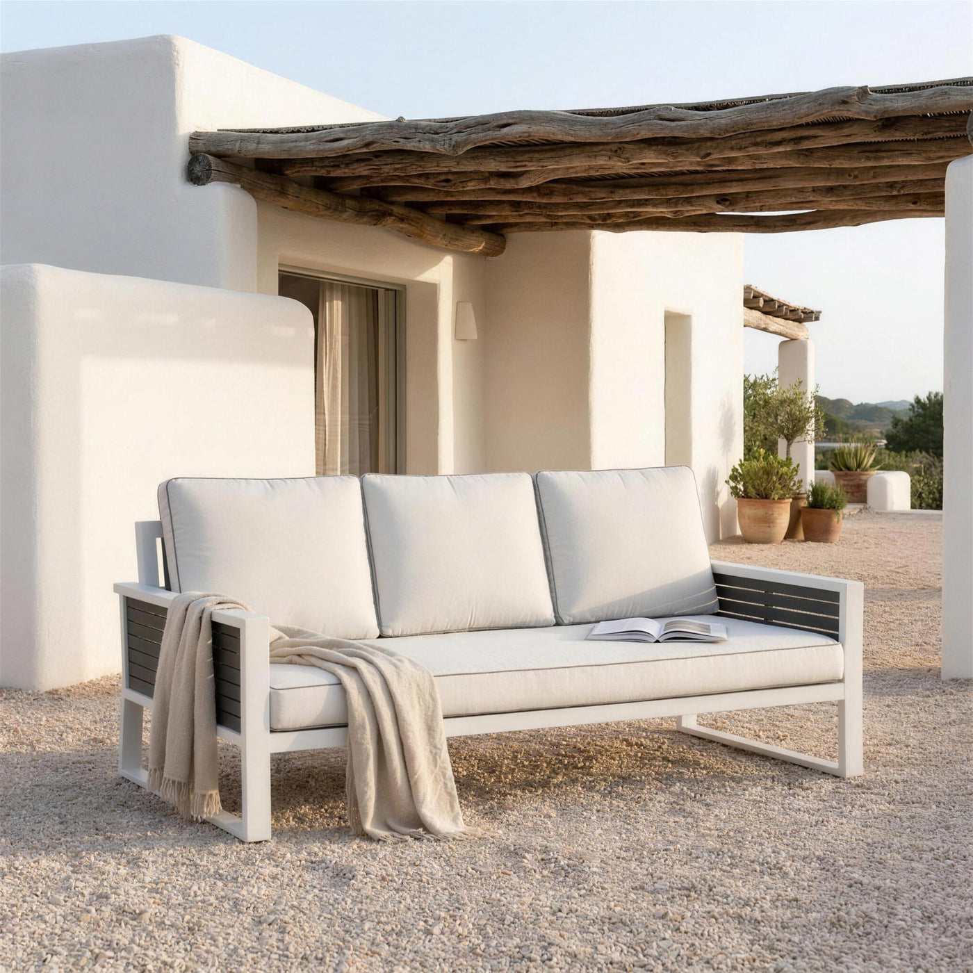 Sofa Diva bicolor de 3 plazas en la terraza de una casa payesa de Ibiza, con muros de cal de aristas redondeadas, pergola de sabina y grava clara