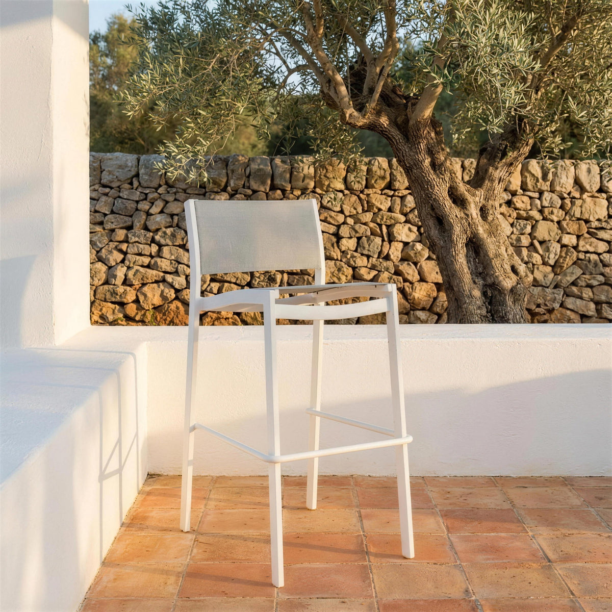 Taburete Etna blanco solo en una terraza de barro cocido de una casa mallorquina, junto a un muro de piedra seca y un olivo viejo. Se vende solo el taburete