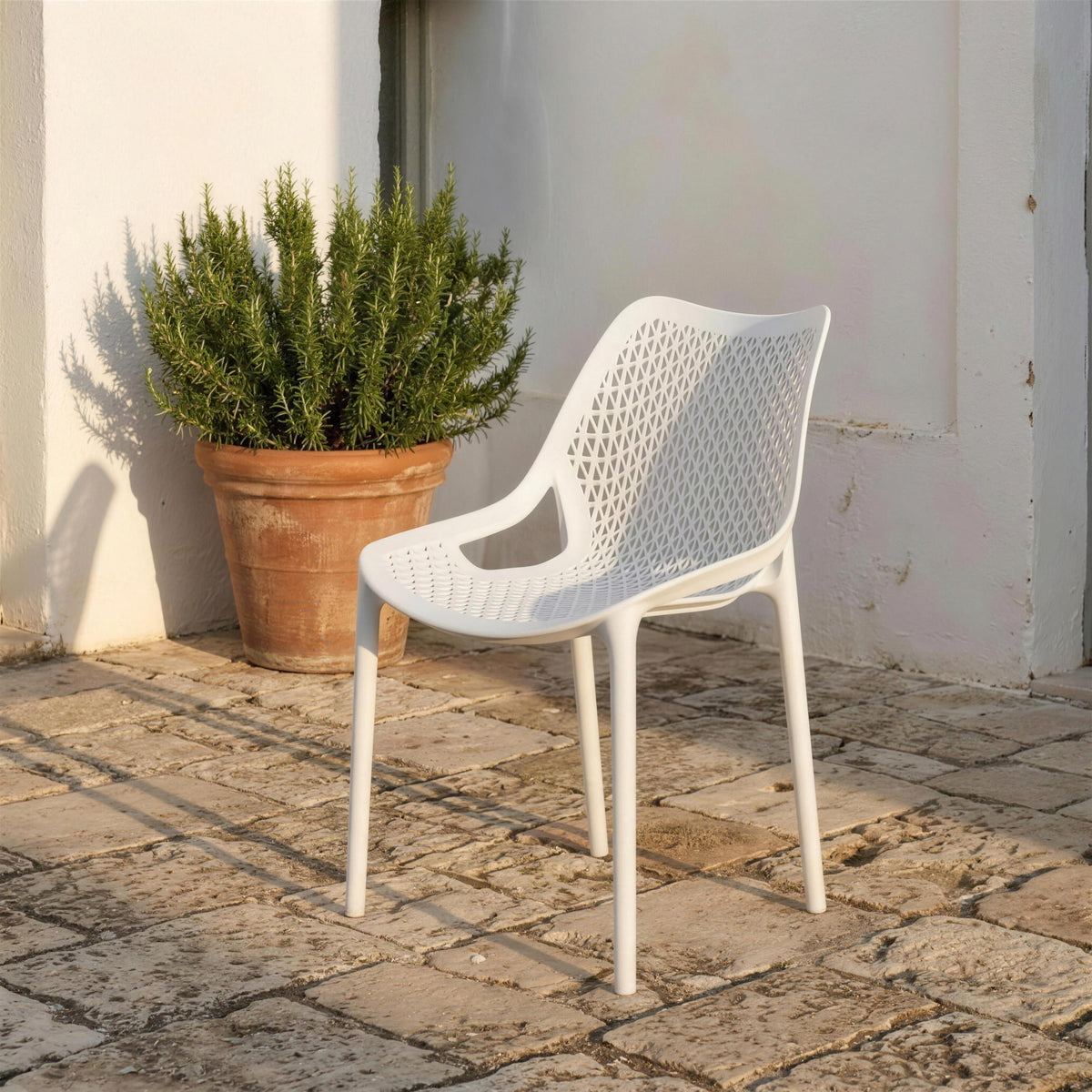 Silla de resina blanca calada, sola en un patio encalado de losas de piedra junto a un romero en tinaja de barro. Se vende solo la silla