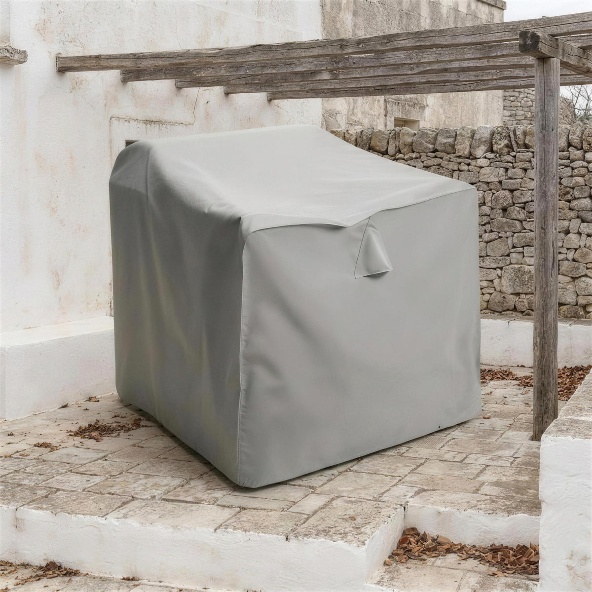 Funda protectora gris cubriendo un sofa en una terraza encalada al final de la temporada, bajo una pergola de madera desnuda. Se vende solo la funda