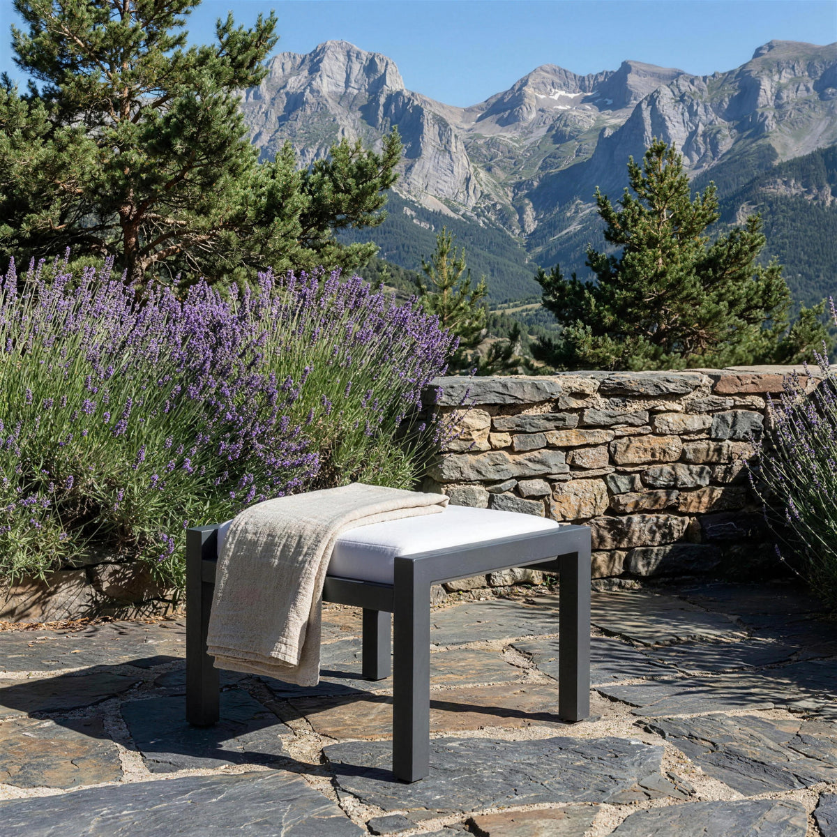 Reposapies Standard XL solo en una terraza de pizarra del Pirineo aragones, junto a un muro de piedra seca con lavanda y los picos rocosos al fondo, con una manta de lino doblada