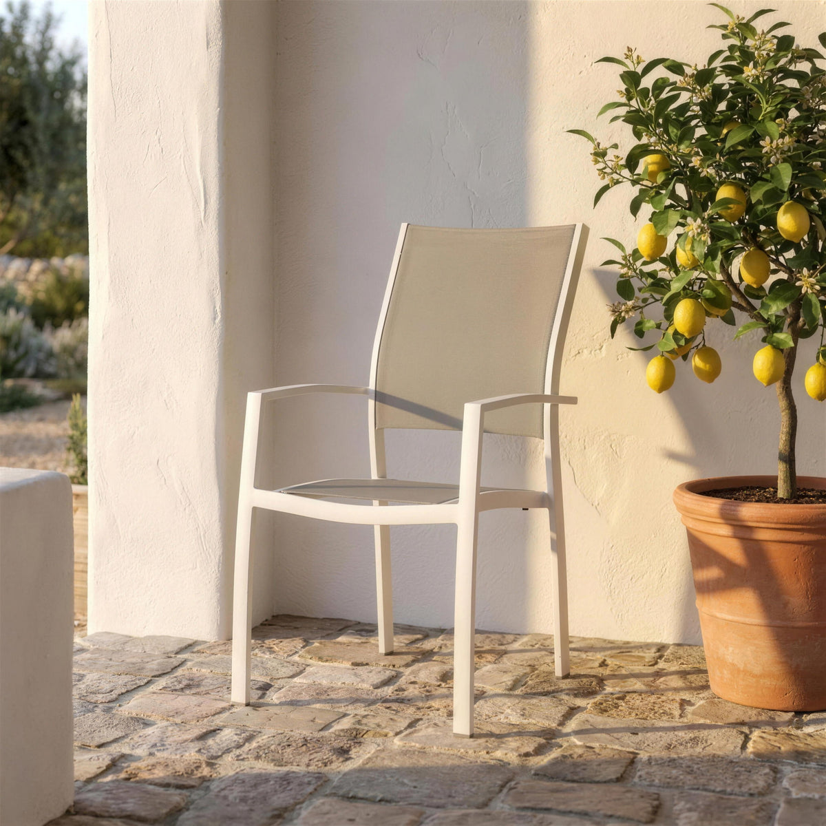 Silla de exterior blanca de respaldo alto, sola en el suelo de piedra de un porche encalado junto a un limonero en maceta. Se vende solo la silla