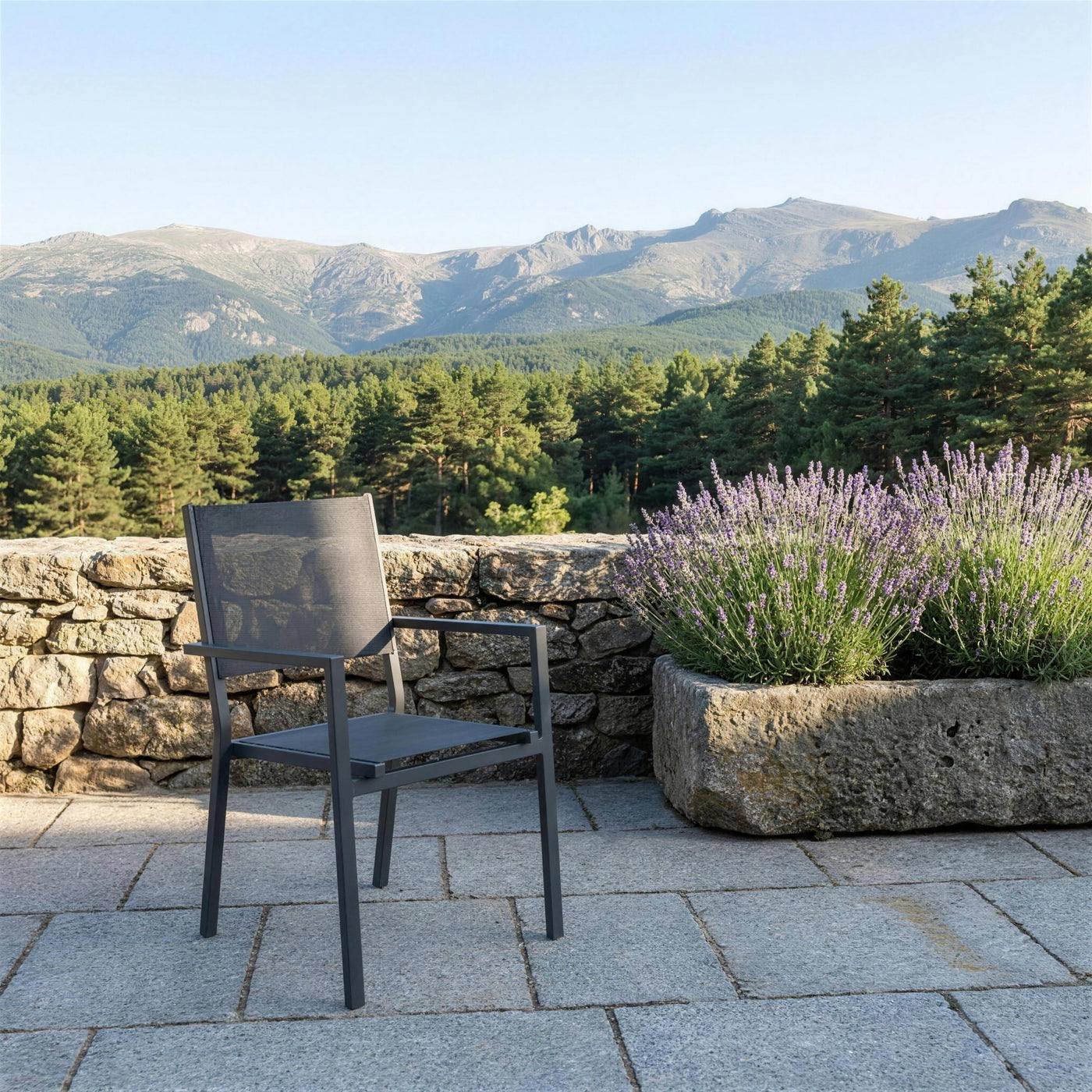 Silla Corcega antracita sola en una terraza de sillar granitico de Segovia, con lavanda en un pilon de piedra y la sierra de Guadarrama al fondo