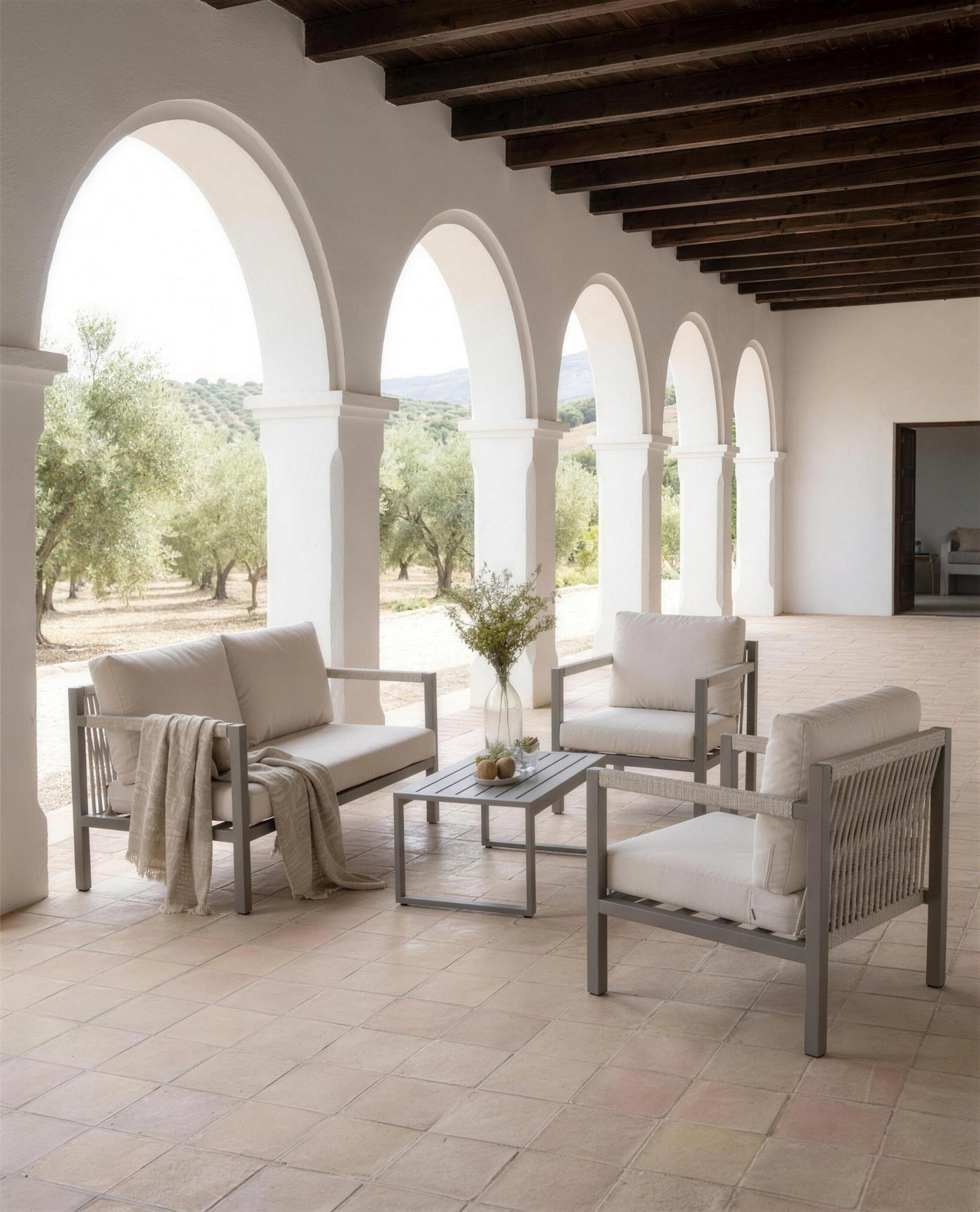Sofa y sillones de exterior en la galeria de arcos encalados de un cortijo andaluz, abierta al olivar