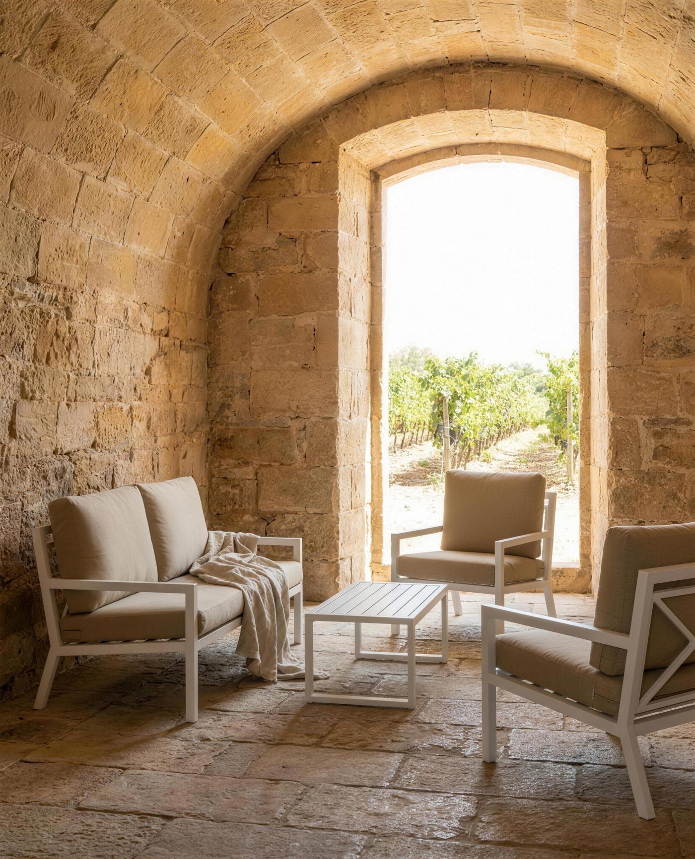 Sofa y sillones Dounvil en una sala abovedada de arenisca con un arco abierto al vinedo
