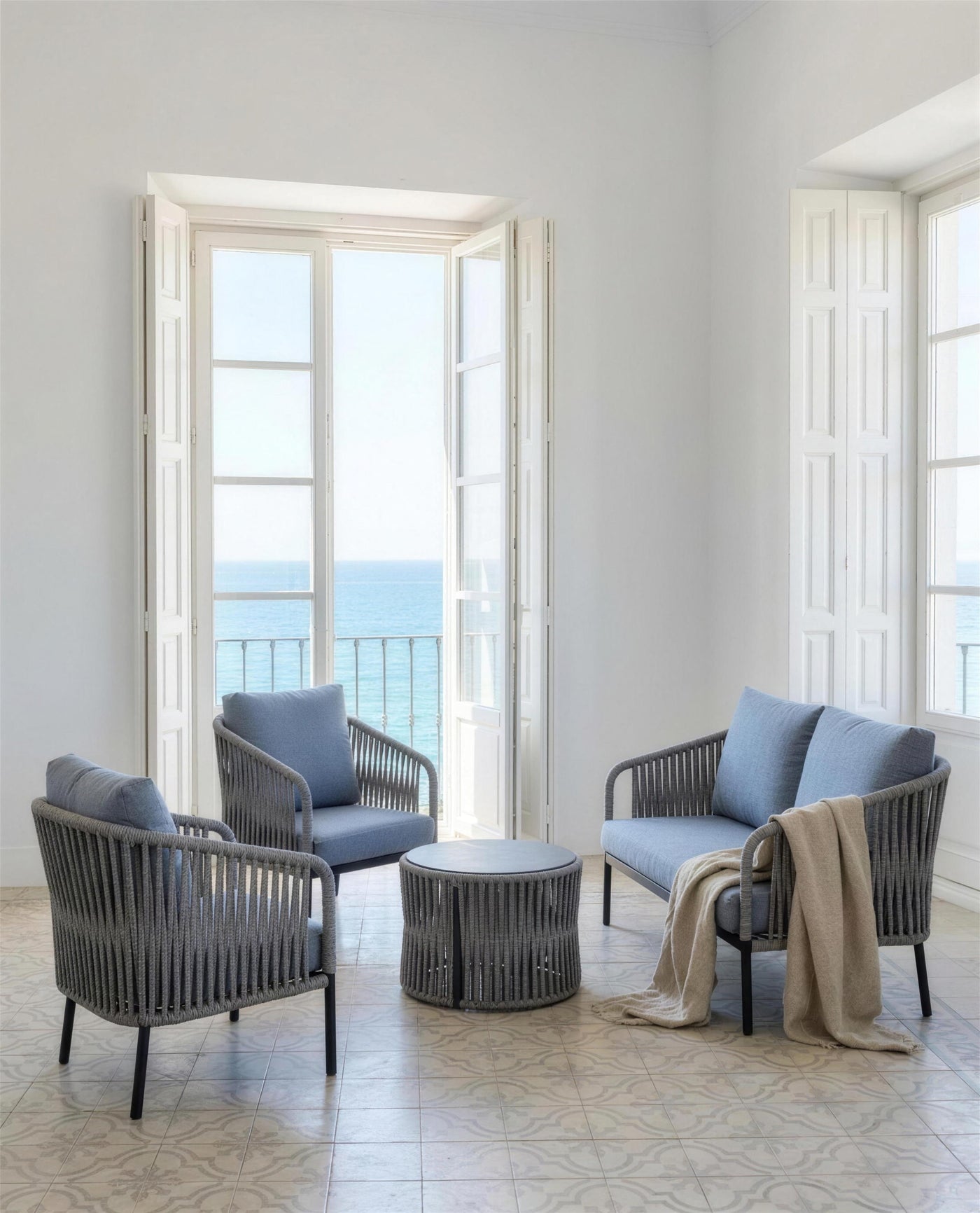 Sofa y sillones Yina de cojines azules en un salon de baldosa hidraulica con el balcon abierto al mar