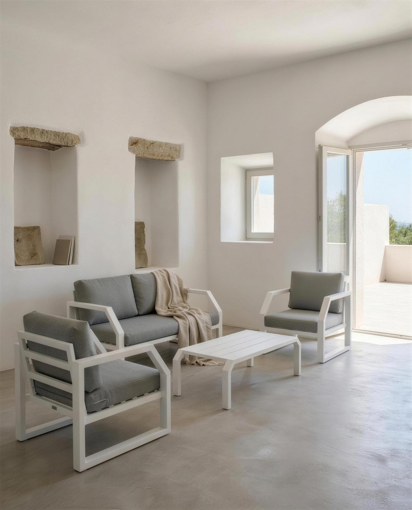 Sofa y sillones Bellagio blancos en una sala encalada con hornacinas de piedra y suelo de microcemento