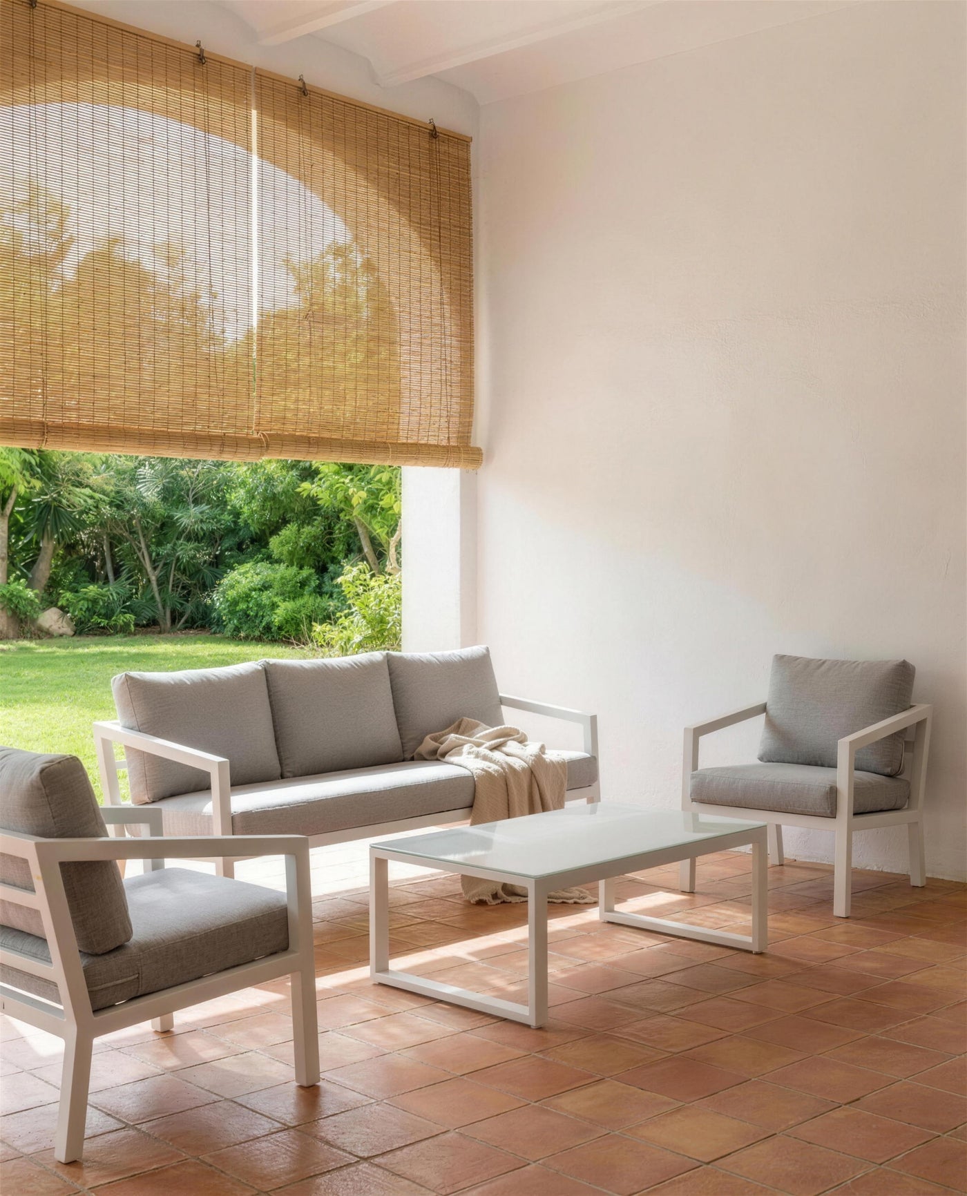 Sofa y sillones Acapulco blancos bajo un porche encalado con persiana de esparto, abierto al jardin
