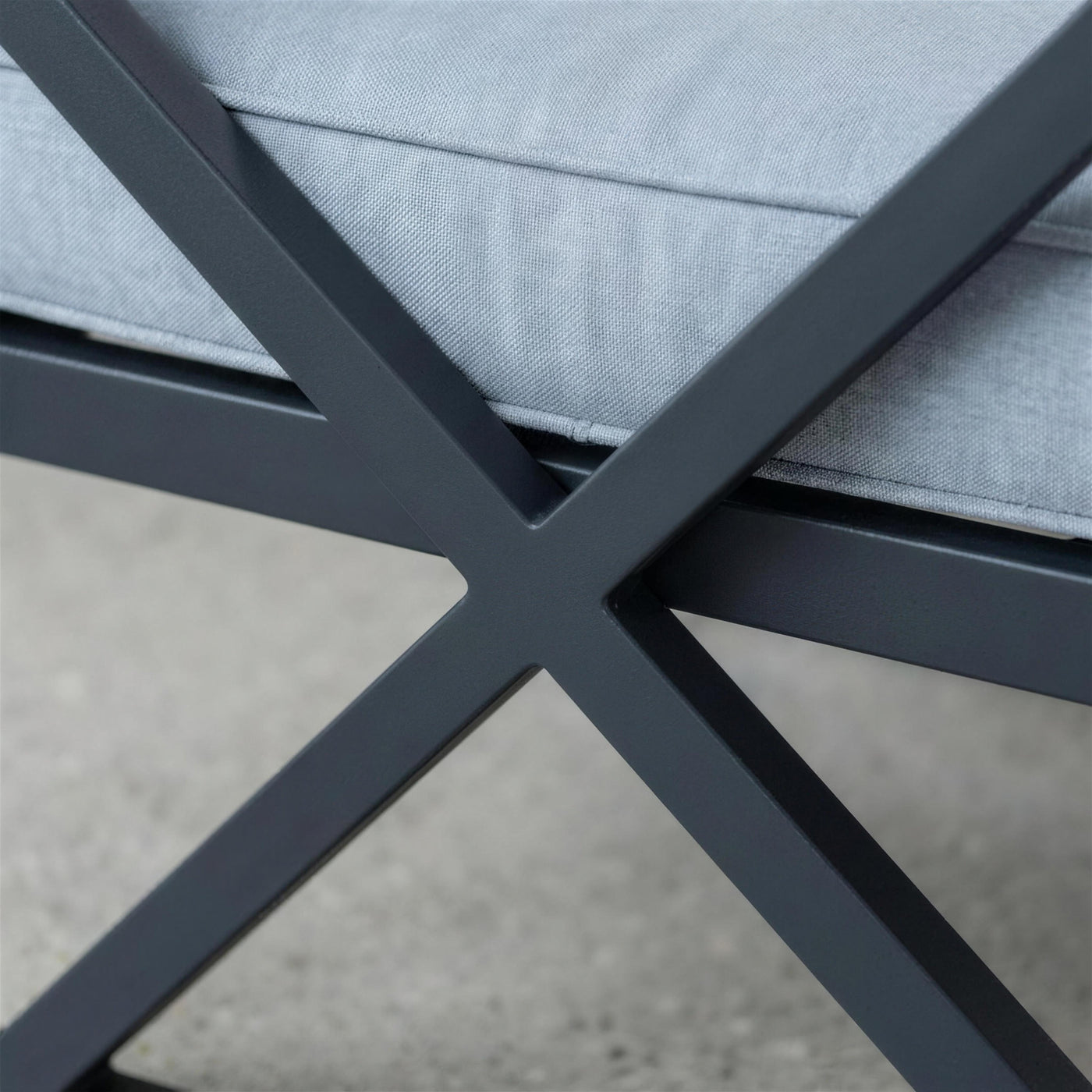 Detalle del aspa en X de aluminio antracita mate del lateral del sillón junto a la costura del cojín azul grisáceo