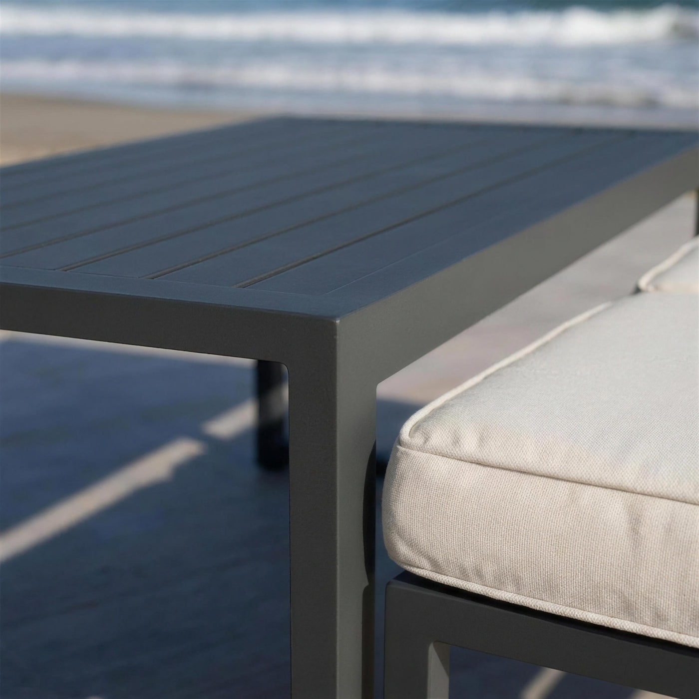 Detalle de las lamas de aluminio antracita de la mesa Adel-30 junto al canto de un cojin blanco crudo