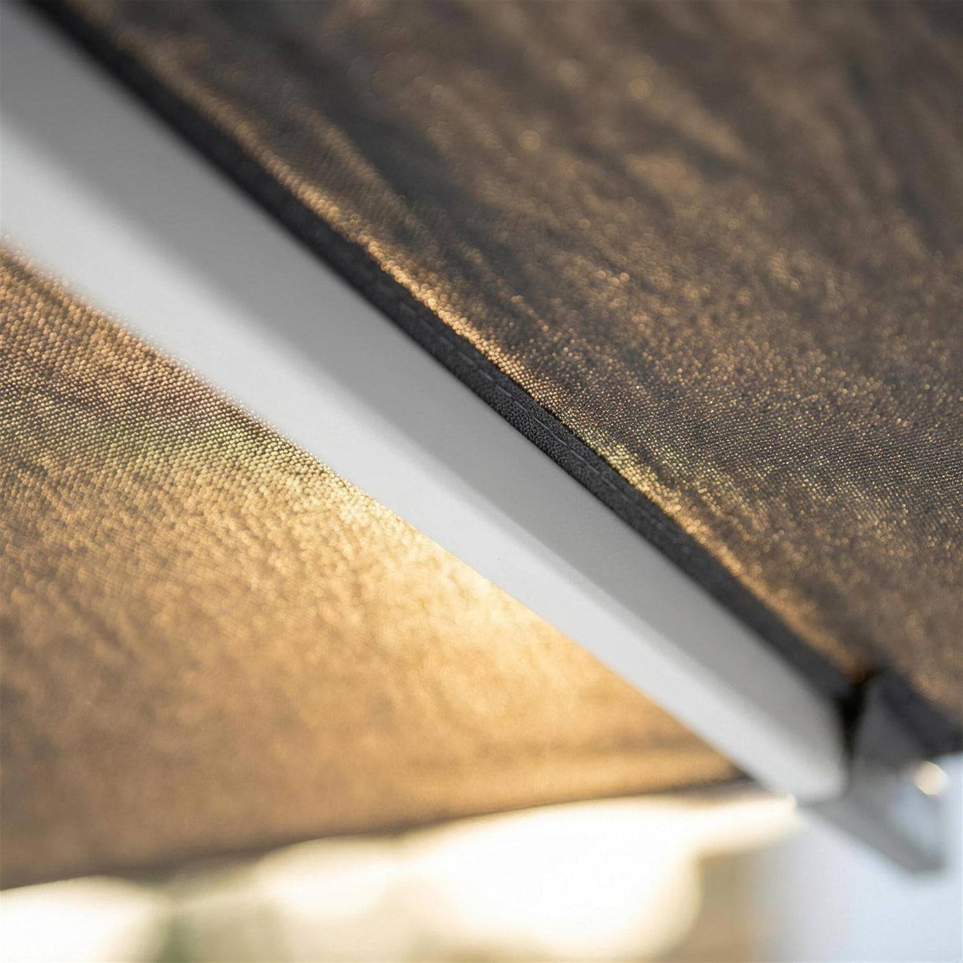 Detalle de la varilla de aluminio blanco y la lona antracita tensada, con el sol atravesando la trama del tejido