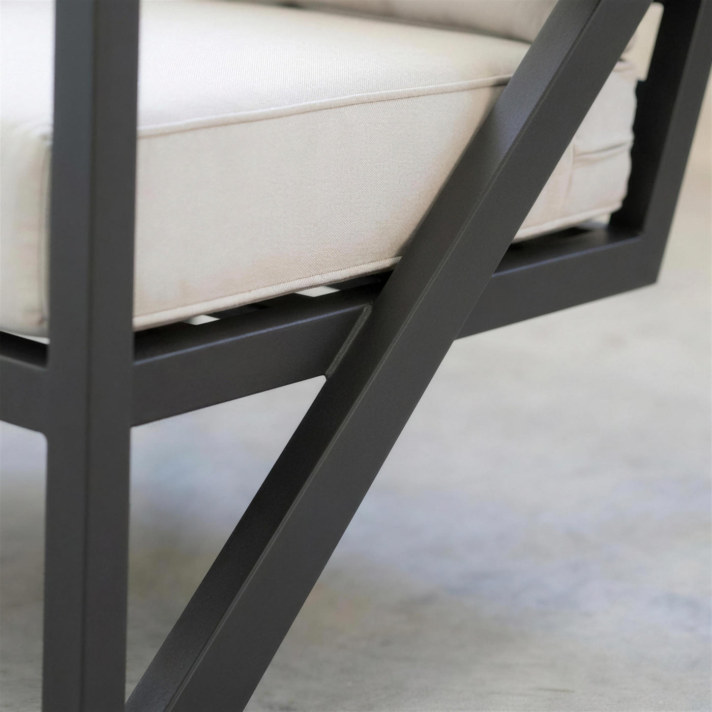 Detalle del travesaño diagonal en V de aluminio antracita del sillón junto a la costura del cojín crudo