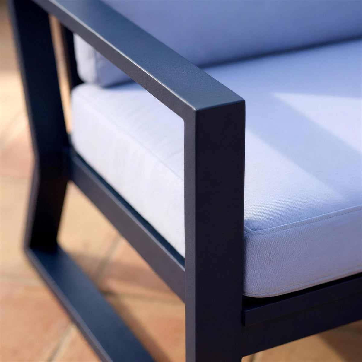 Detalle de la esquina donde el brazo de aluminio azul marino mate se une con la pata delantera inclinada del sillon, junto al canto del cojin azul lavanda