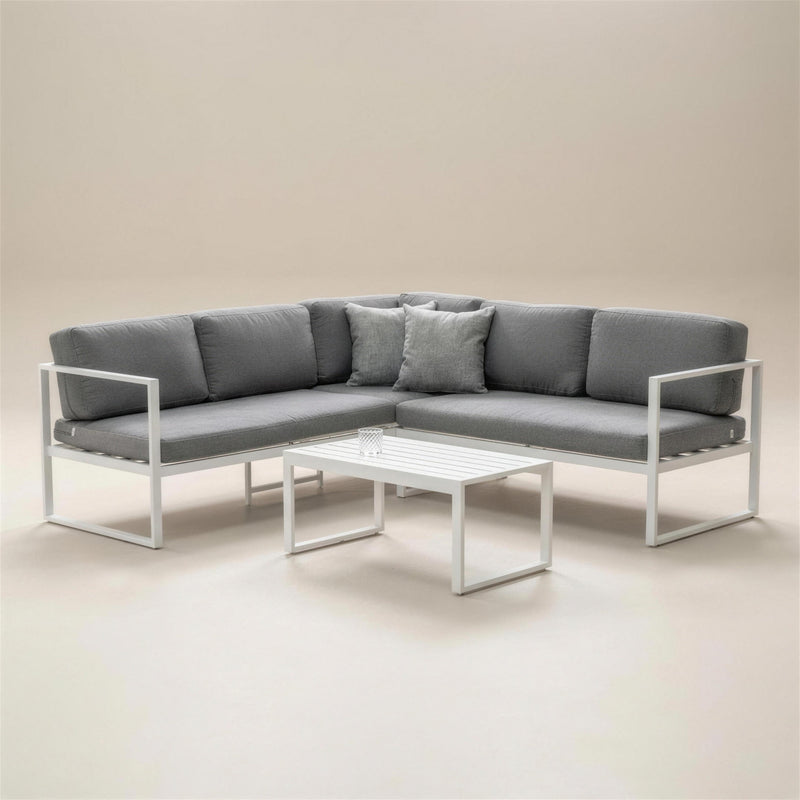Set rinconera de exterior Adel-7 en aluminio blanco con cojines gris marengo, dos cojines de acento y mesa de centro baja, sobre fondo neutro