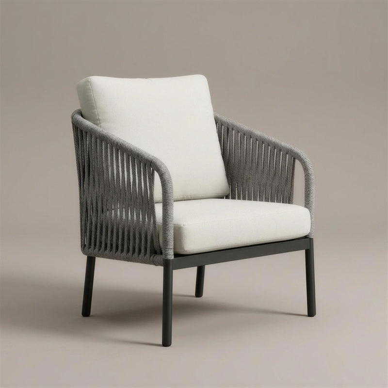 Sillon de exterior Yina con respaldo y brazos de cuerda trenzada gris sobre aluminio antracita y cojines crudo, 77x72x83 cm, sobre fondo neutro
