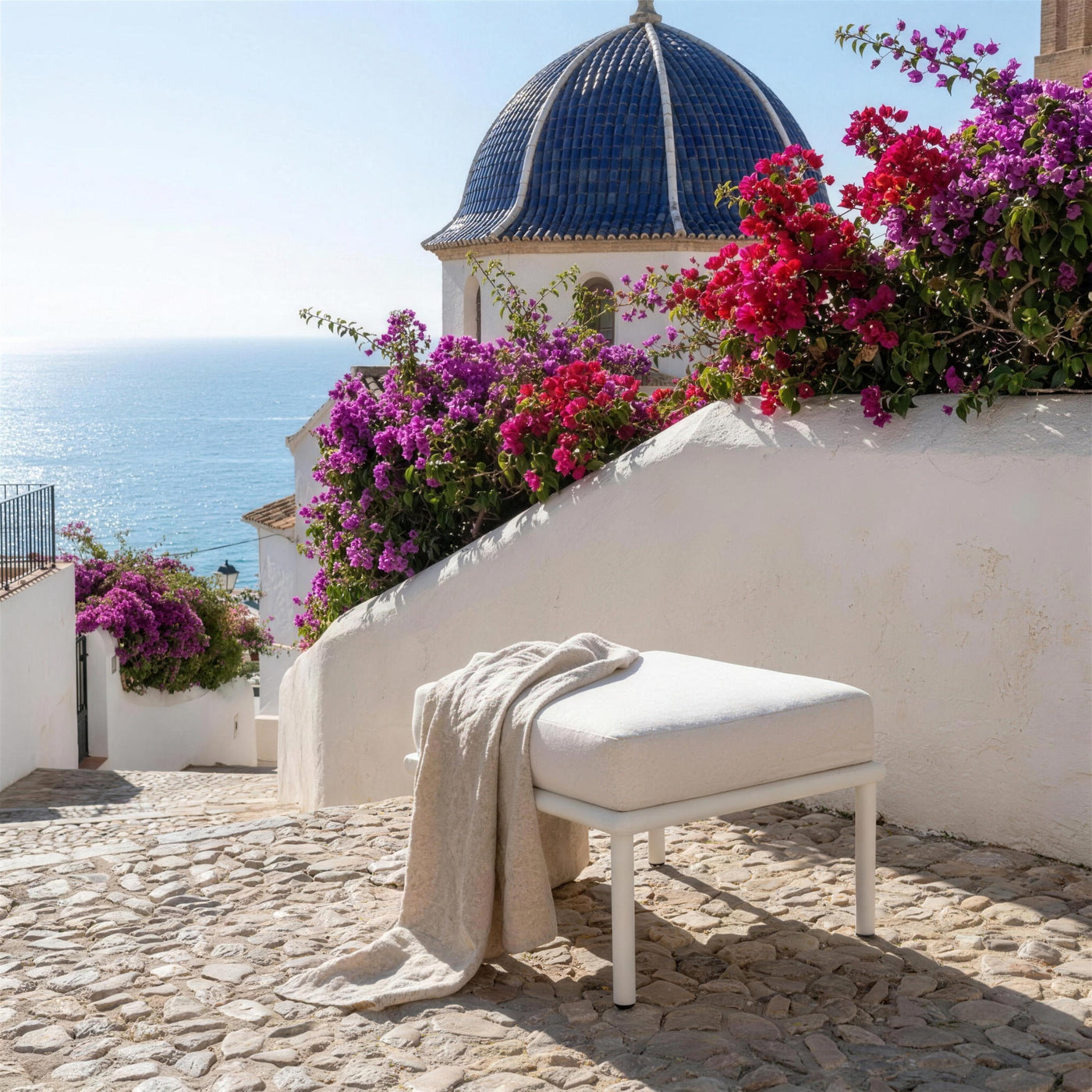 Reposapies Cloe solo en una terraza encalada de Altea, junto a una calle empedrada que baja al mar, con buganvilla y la cupula de teja azul