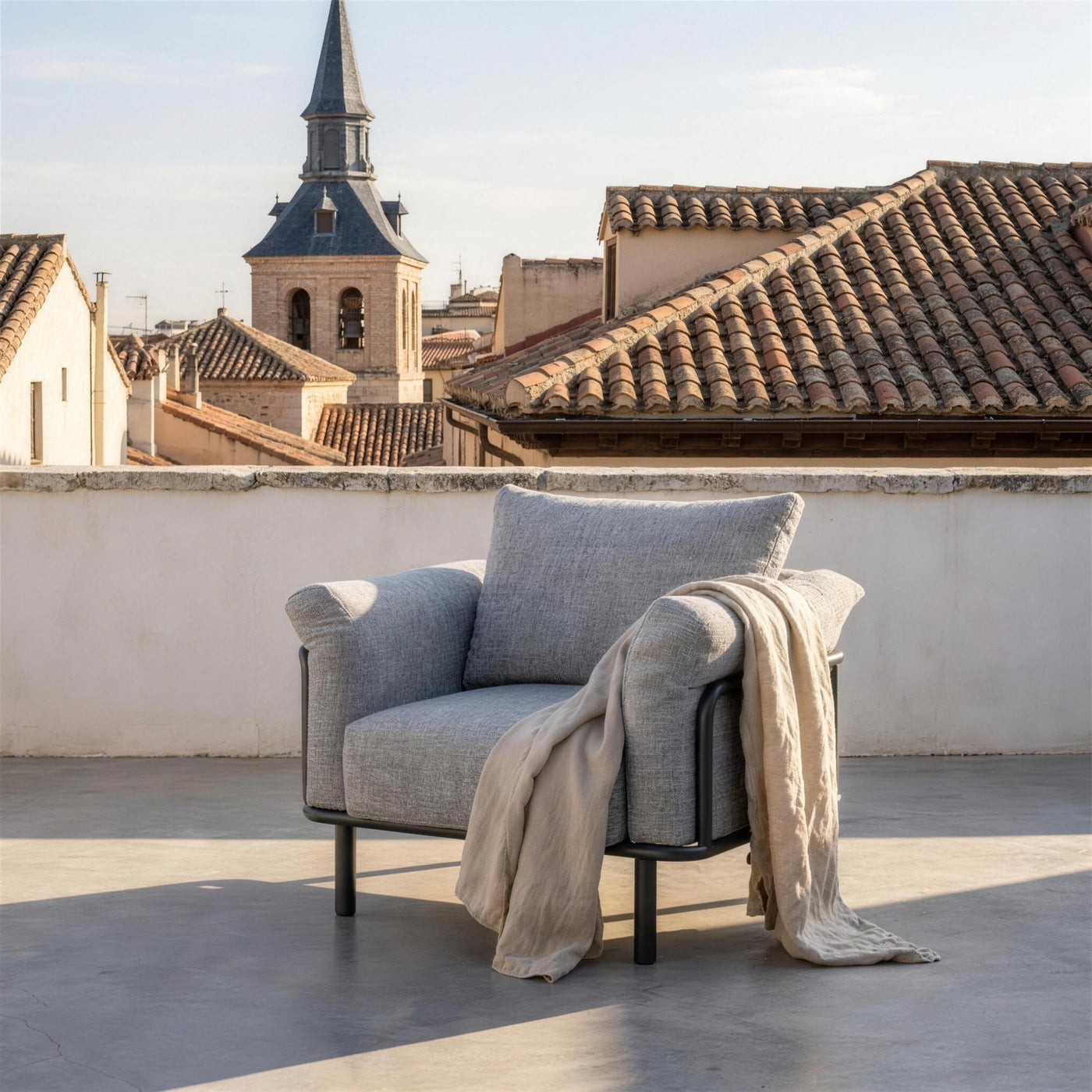 Sillon gris en una azotea del Madrid antiguo, con parapeto encalado y los tejados de teja arabe y una torre con chapitel de pizarra al fondo