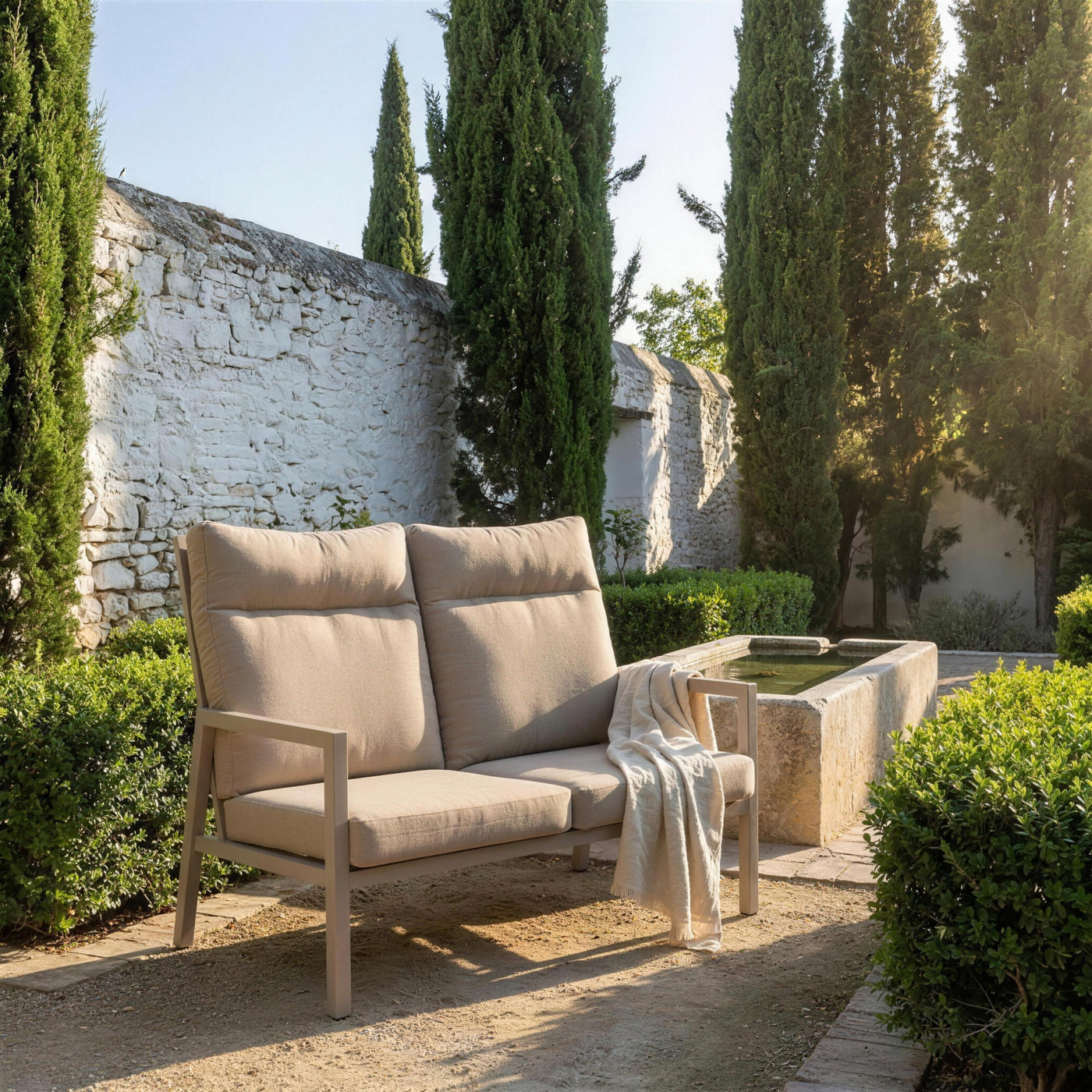 Sofa Haston de 2 plazas de respaldo alto en el jardin de un carmen del Albaicin granadino, junto a una alberca de piedra, con cipreses y setos de mirto