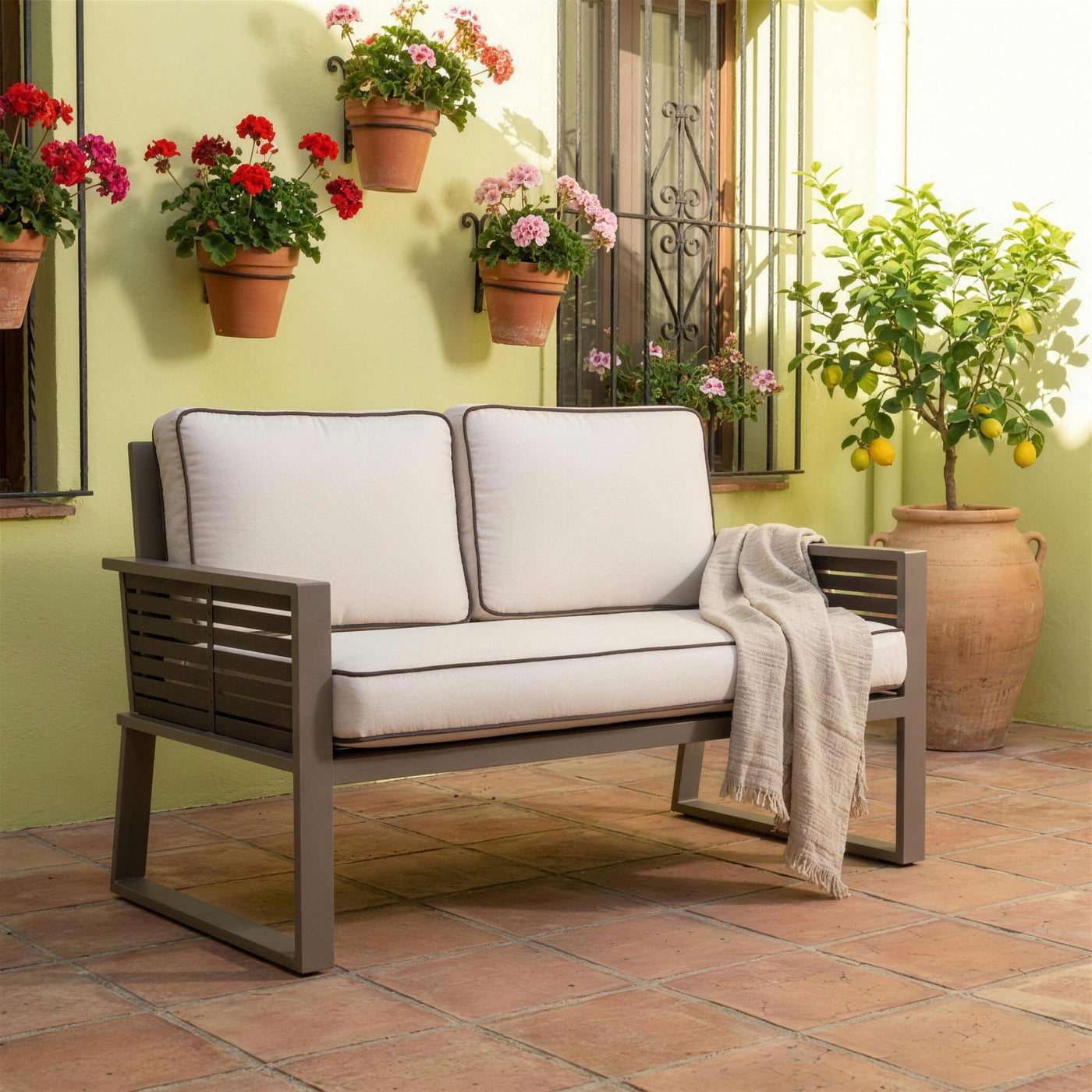 Sofa Diva bicolor de 2 plazas en un patio cordobes, con geranios en macetas de barro colgadas del muro, reja de forja y un limonero en tinaja