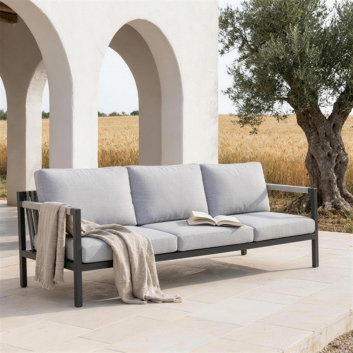 Sofa Damasco de 3 plazas en la terraza de caliza de un cortijo de la campina sevillana, bajo arcos encalados, con un olivo viejo y los trigales al fondo