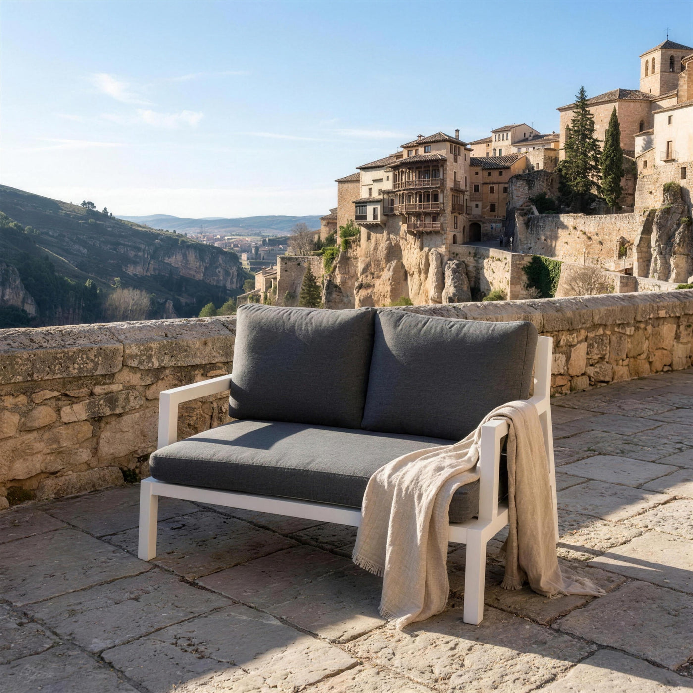 Sofa Leisa de 2 plazas en una terraza de piedra sobre el casco viejo de Cuenca, con las casas colgadas y la hoz del Huecar al fondo