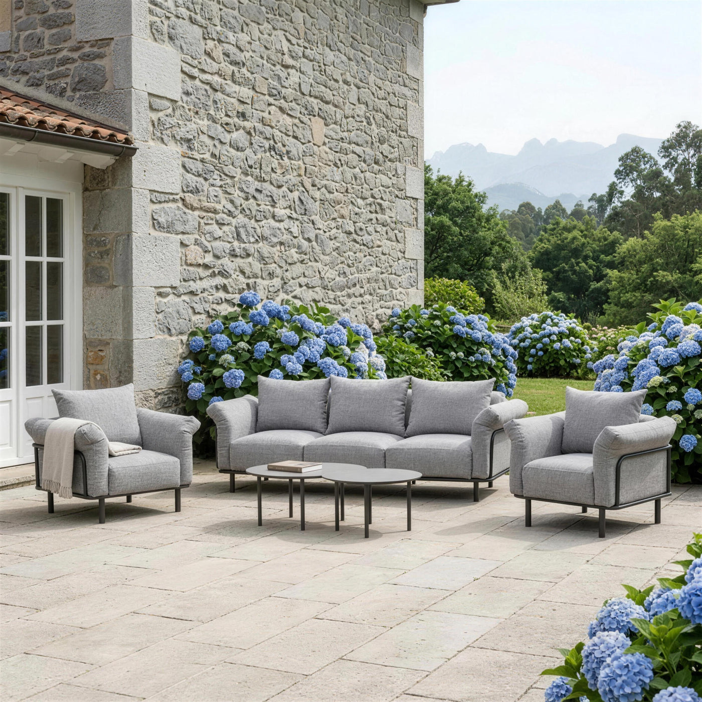 Conjunto de jardin gris en la terraza de losa de piedra de una casona de mamposteria del norte de Espana, entre hortensias azules en flor