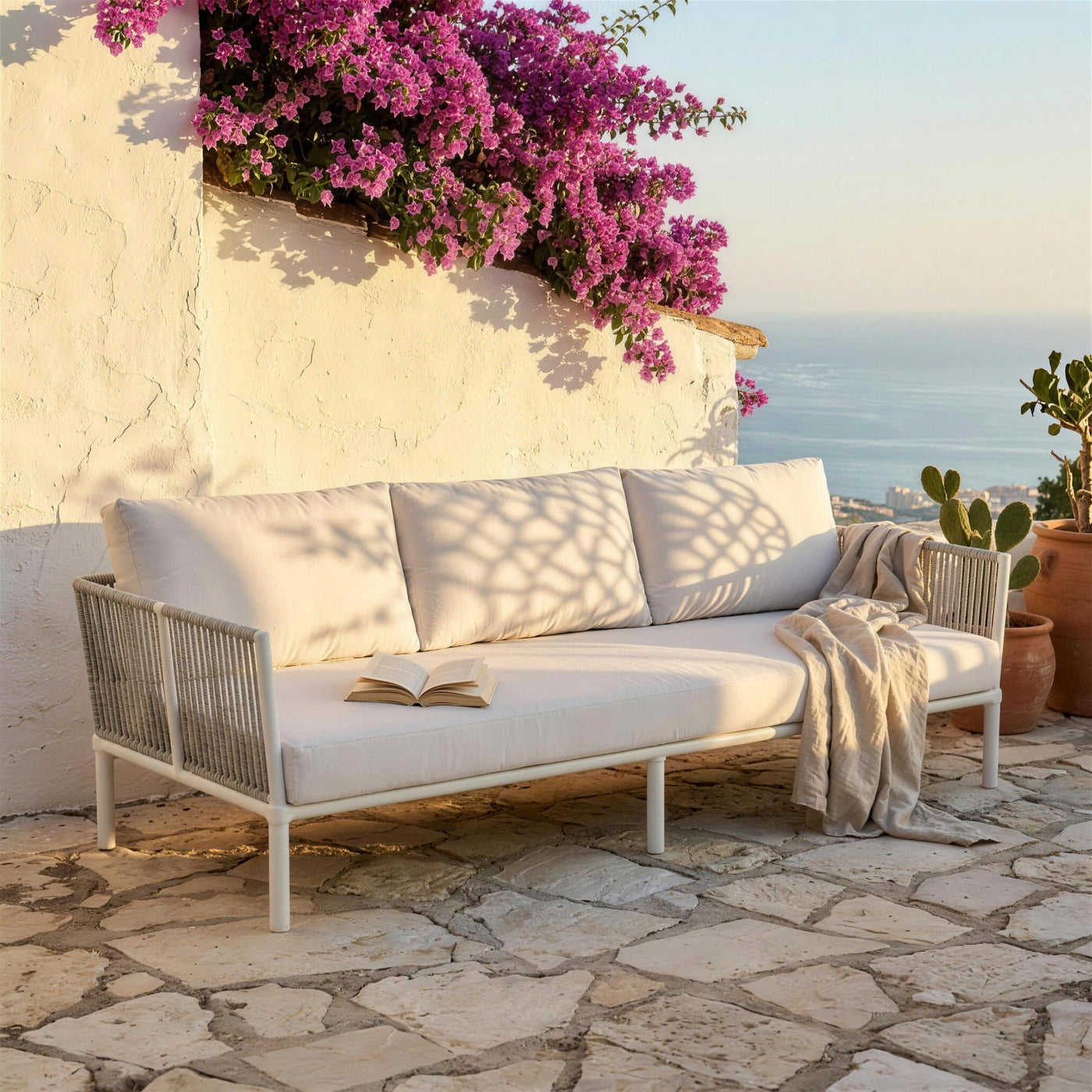 Sofá de terraza blanco en la terraza encalada de una casa malagueña, con buganvilla sobre el muro y el Mediterráneo al fondo