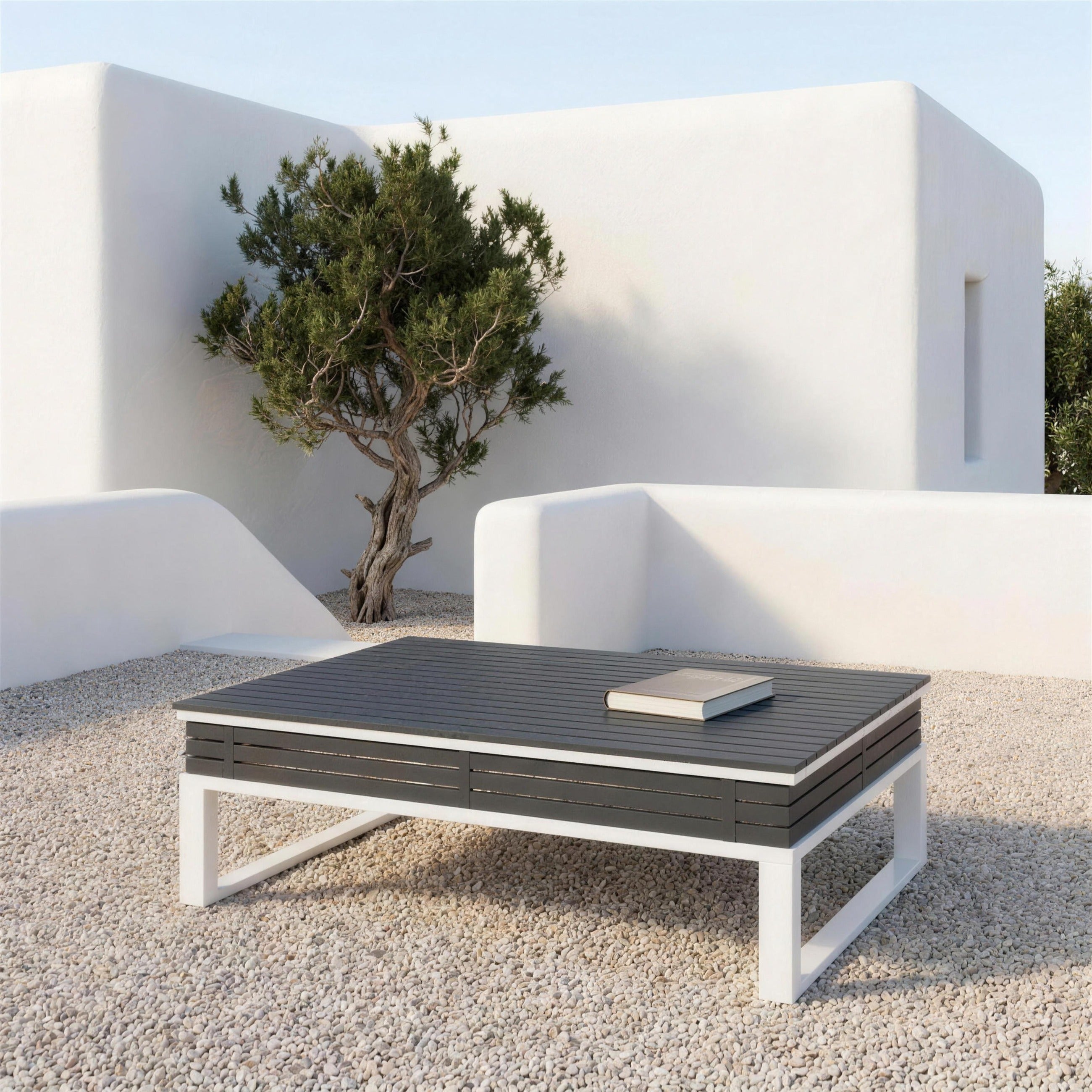 Mesa de centro bicolor sola en la terraza de una casa payesa de Ibiza, sobre grava clara, con muros de cal y una sabina