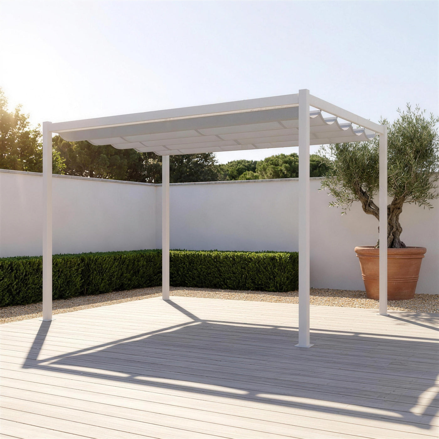 Pergola Venecia blanca sobre tarima en un jardin con muro encalado, seto y un olivo en tinaja, proyectando su sombra