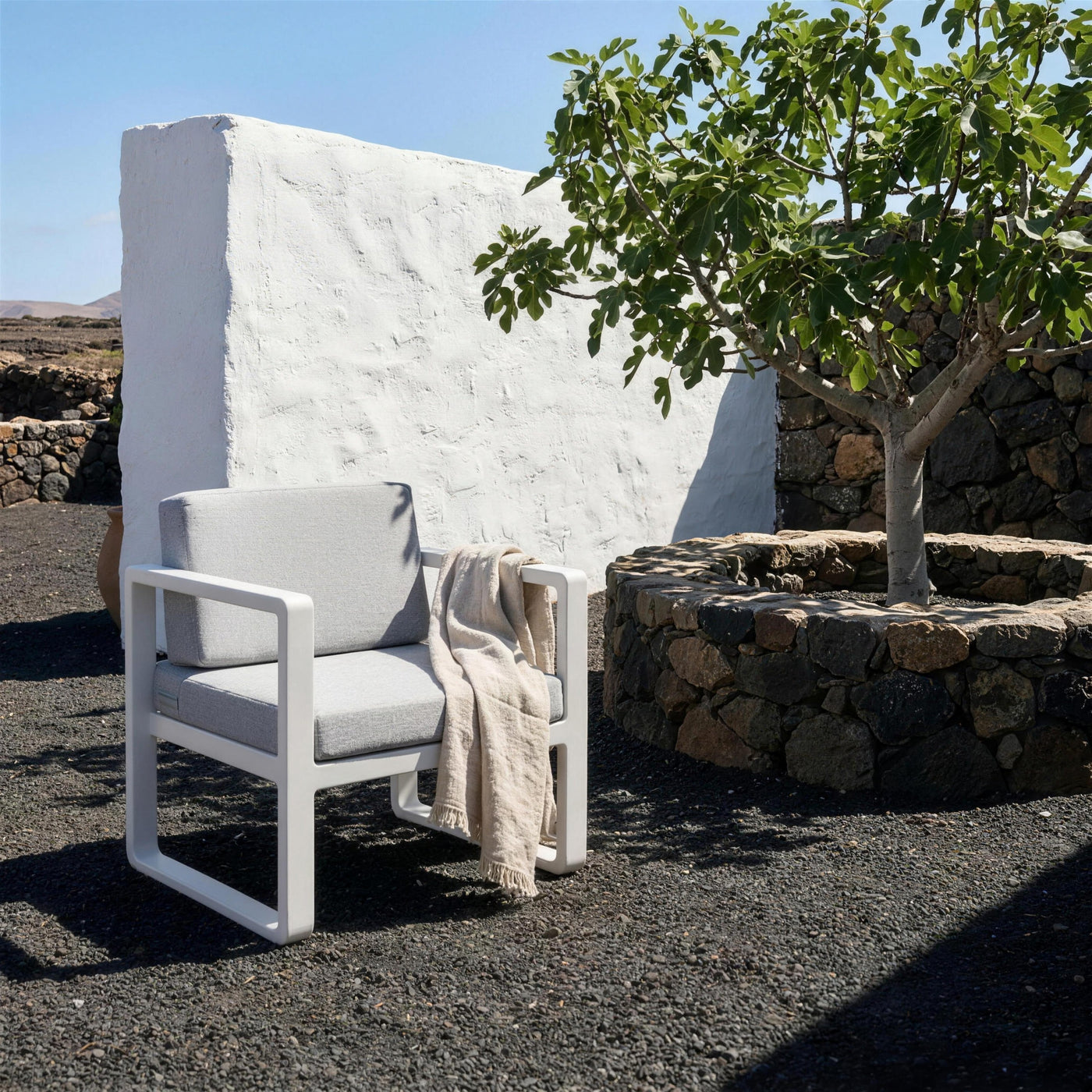 Sillon Odin blanco en una terraza de Lanzarote, con suelo de picon negro, muro encalado y una higuera en su zoco de piedra volcanica
