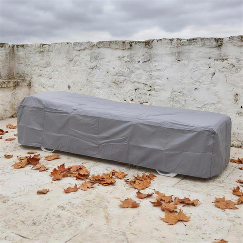 Funda protectora gris cubriendo una tumbona en una terraza encalada en otono, con hojas secas en el suelo de piedra. Se vende solo la funda