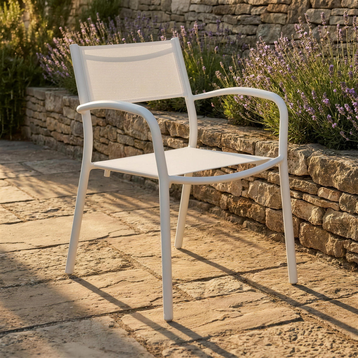 Silla de exterior blanca de aluminio, sola en una terraza de piedra junto a un muro de piedra seca con lavanda. Se vende solo la silla