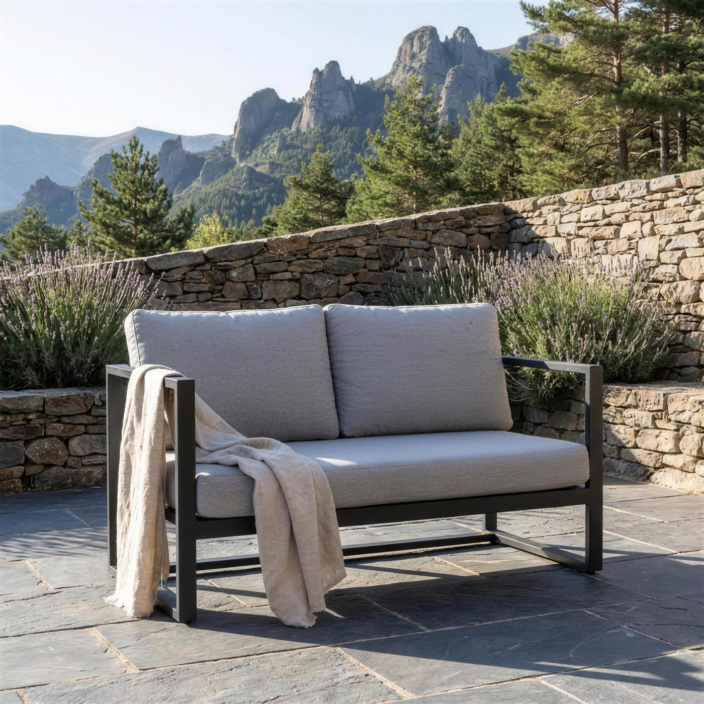 Sofa Manhatan de 2 plazas en una terraza de pizarra del Pirineo aragones, junto a un muro de piedra seca con lavanda, pinos y los picos rocosos al fondo