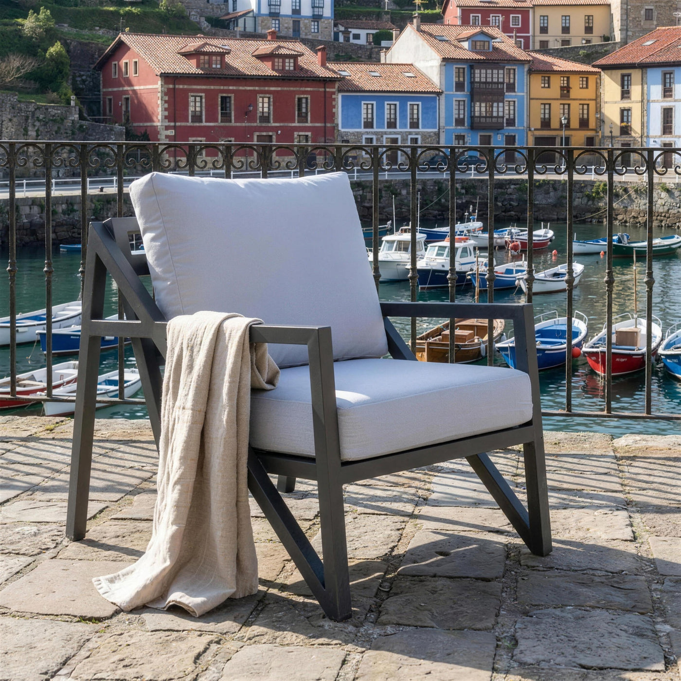 Sillon Albania antracita en una terraza de piedra sobre un puerto pesquero asturiano, con reja de forja, las casas de colores y las barcas abajo