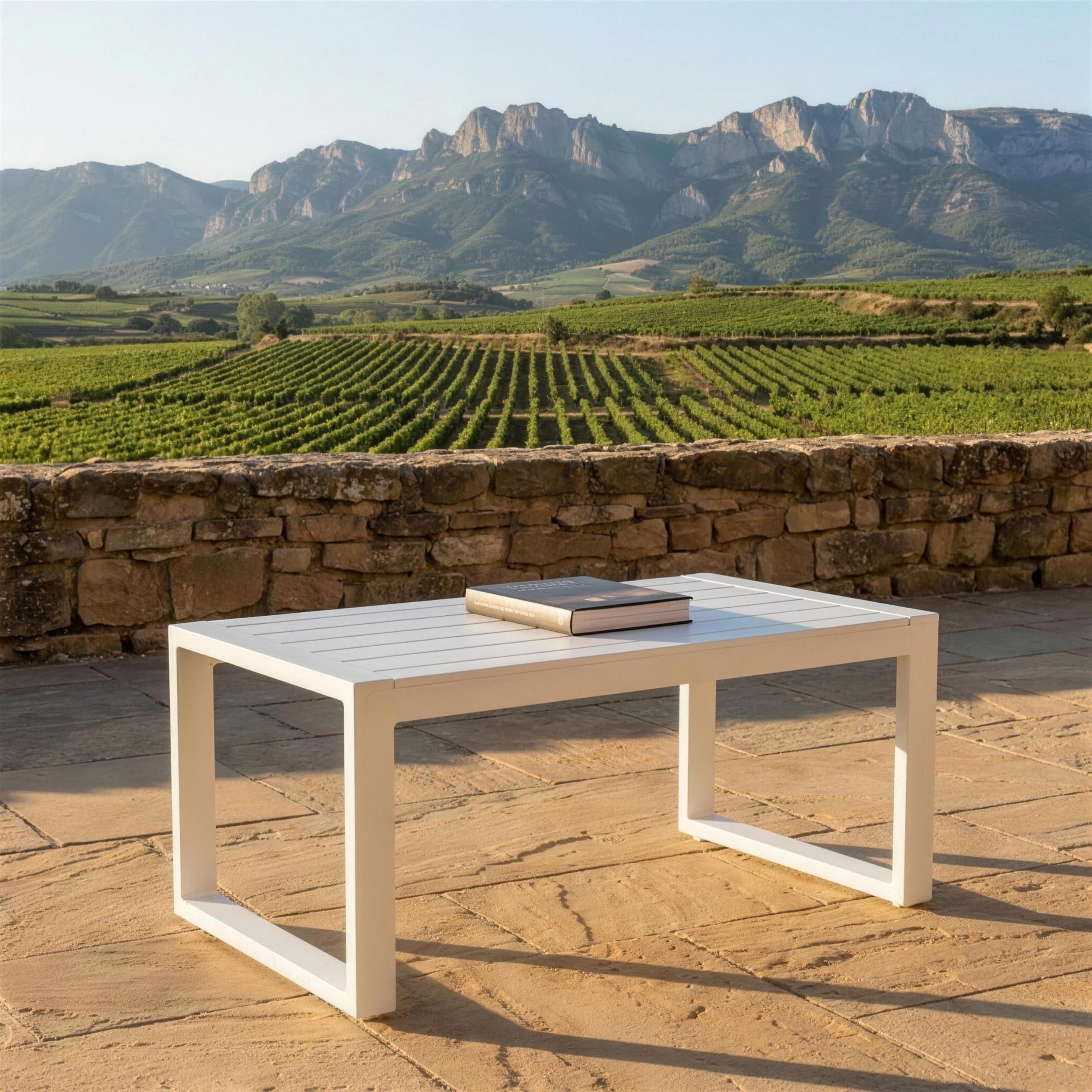 Mesa de centro blanca sola en una terraza de piedra arenisca sobre los vinedos de La Rioja, con la Sierra de Cantabria al fondo
