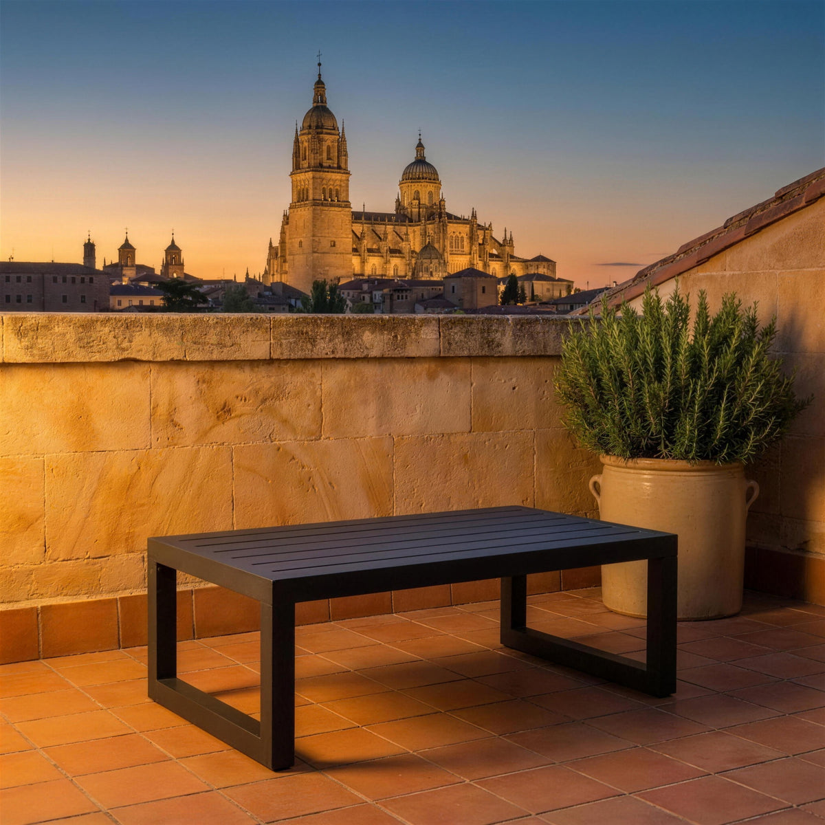 Mesa de centro Universal antracita sola en una azotea de Salamanca, sobre piedra dorada de Villamayor, con las torres de la catedral al atardecer y romero en una tinaja de gres