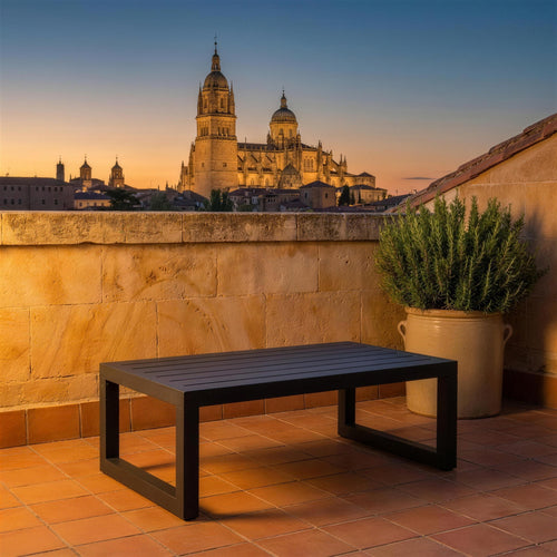 Mesa de centro Universal antracita sola en una azotea de Salamanca, sobre piedra dorada de Villamayor, con las torres de la catedral al atardecer y romero en una tinaja de gres