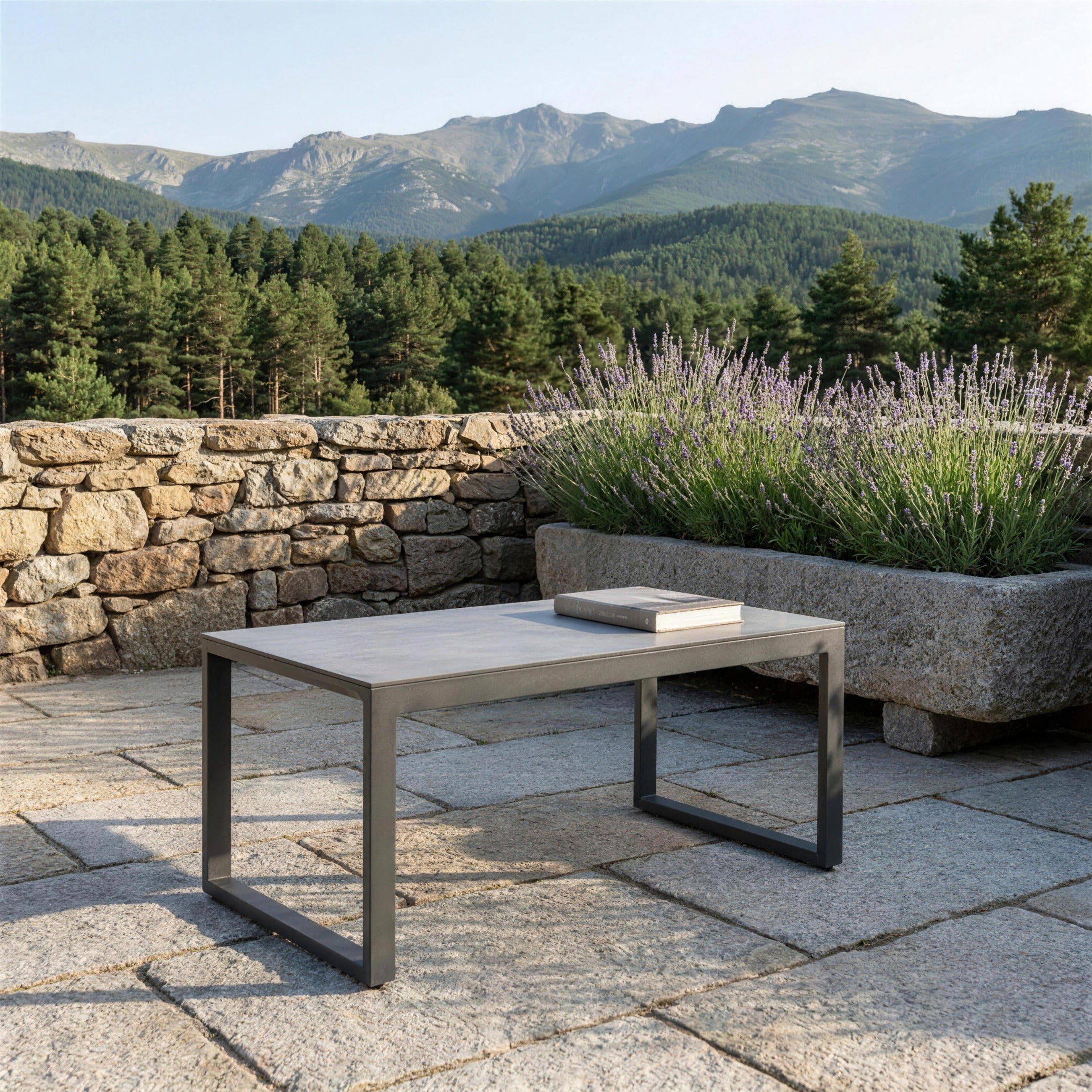 Mesa de centro antracita con tablero de cemento sola en una terraza de sillar granitico de Segovia, con lavanda en un pilon de piedra y la sierra al fondo