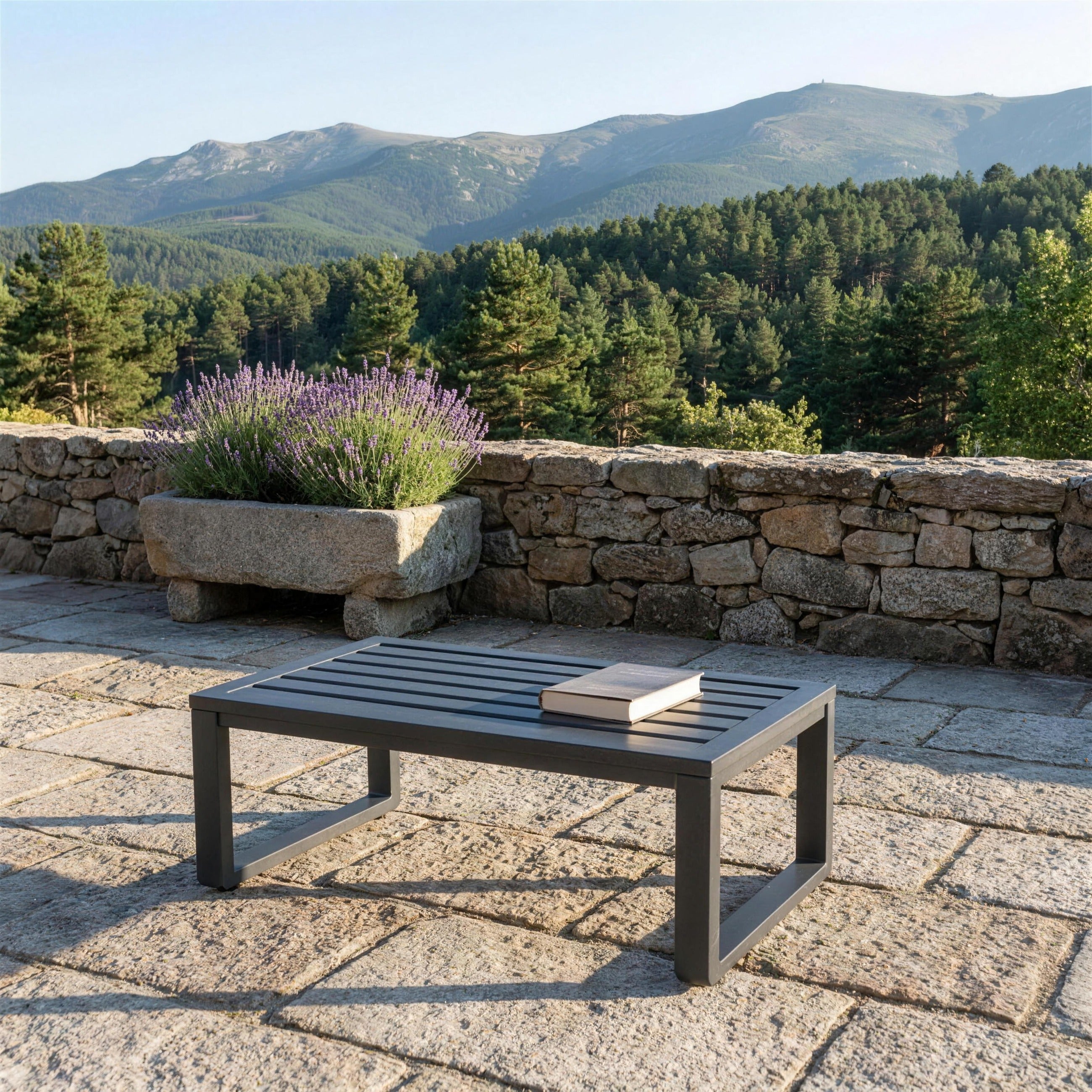Mesa de centro Saipros antracita sola en una terraza de sillar granitico de Segovia, con lavanda en un pilon de piedra y la sierra al fondo