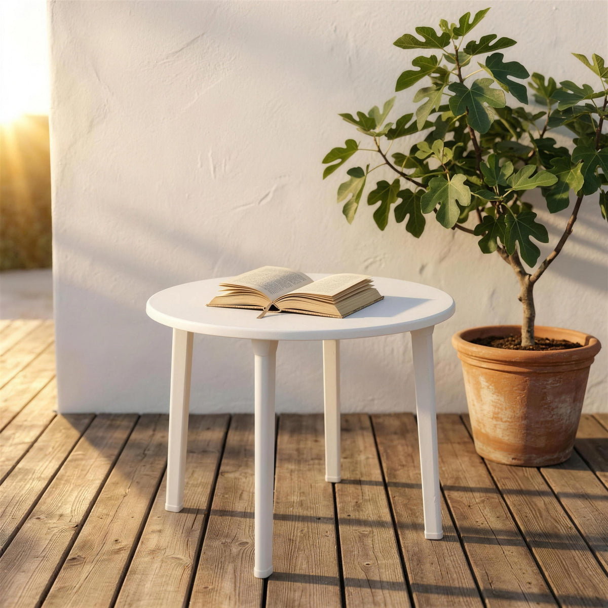 Mesa redonda blanca de exterior, sola en una terraza de tarima de madera junto a una higuera en maceta y un muro encalado. Se vende solo la mesa, sin sillas