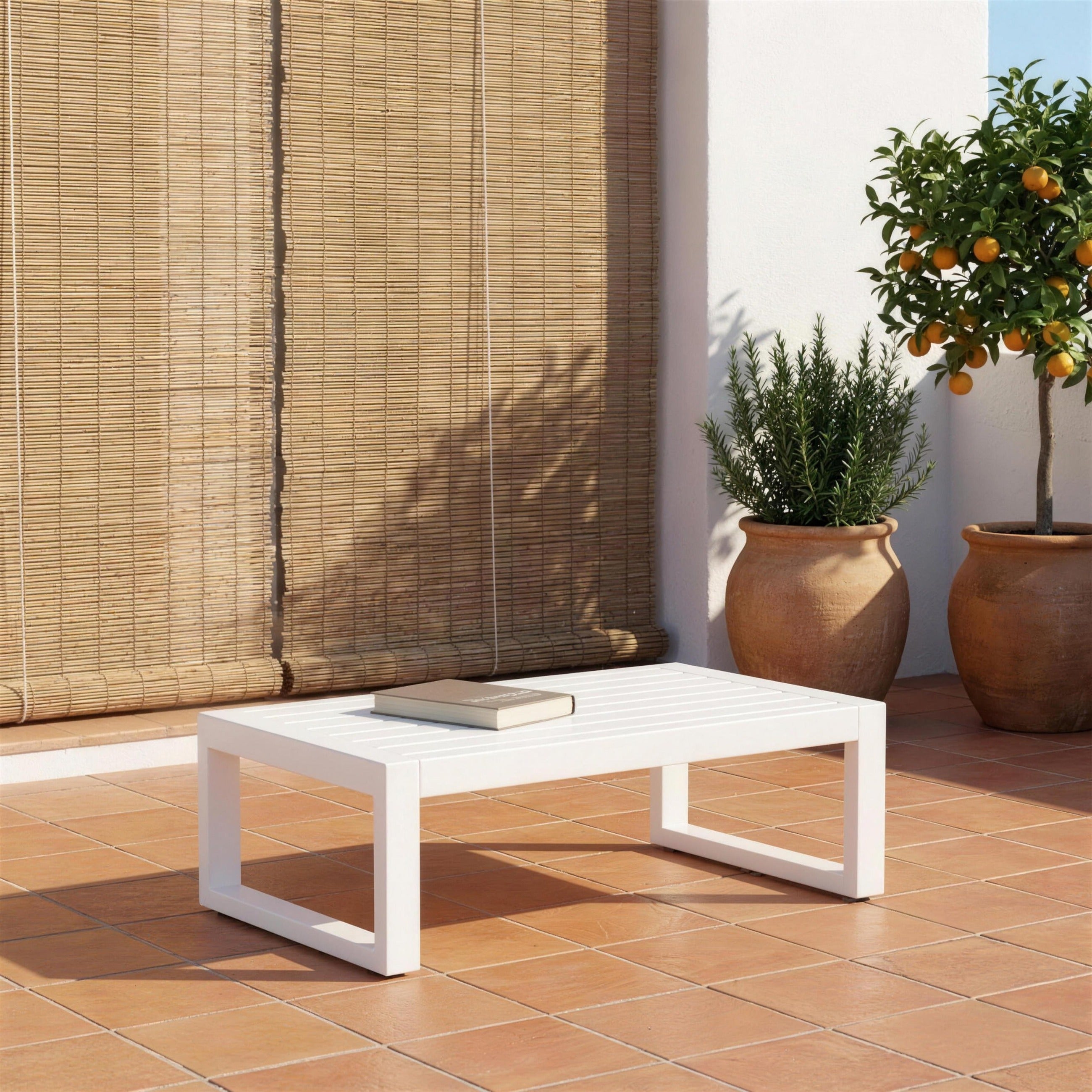 Mesa de centro Saipros blanca sola en una terraza valenciana de suelo de barro, con persiana de esparto, romero y un naranjo en tinaja