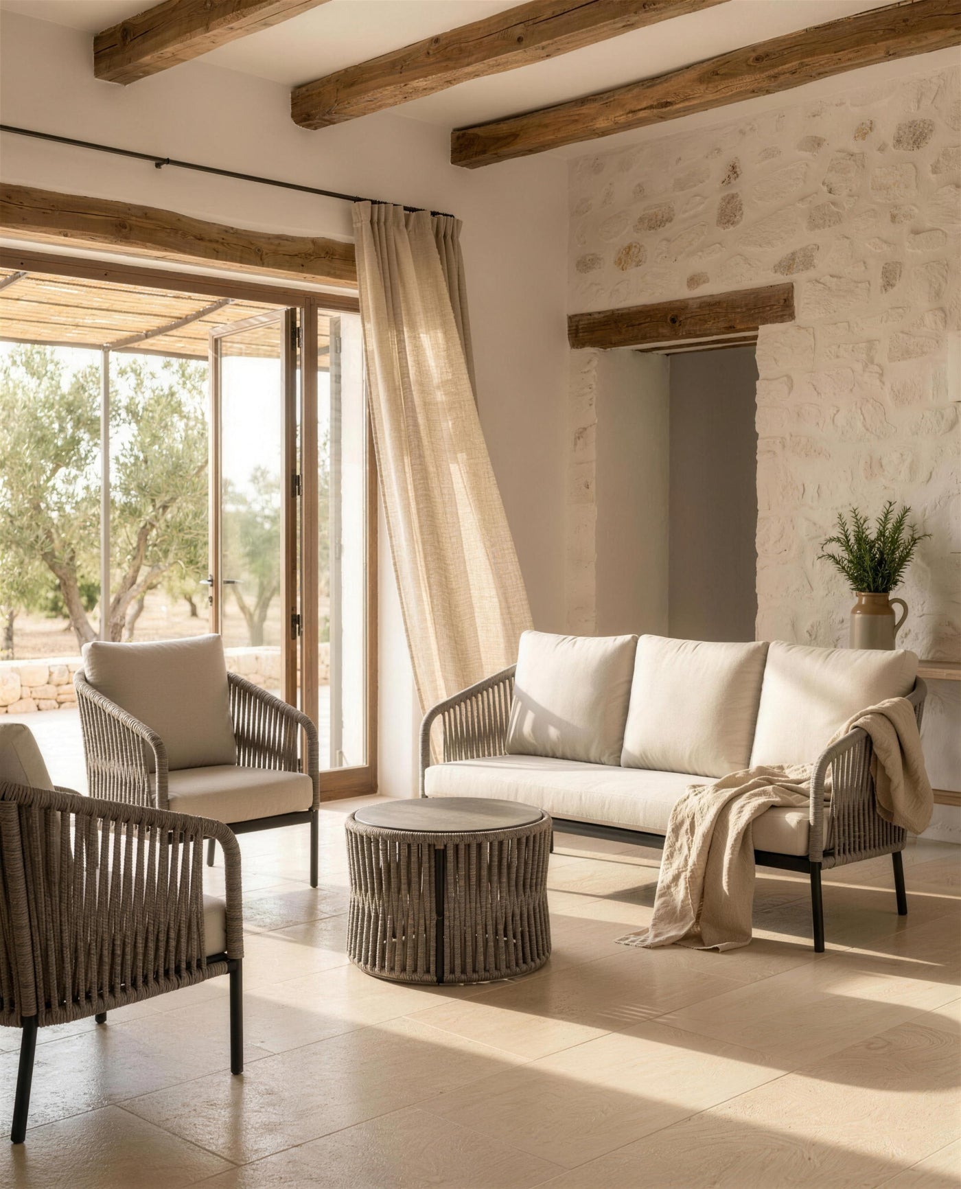 Sofa y sillones Yina en una sala payesa encalada con vigas de madera y cortina de lino abierta al olivar
