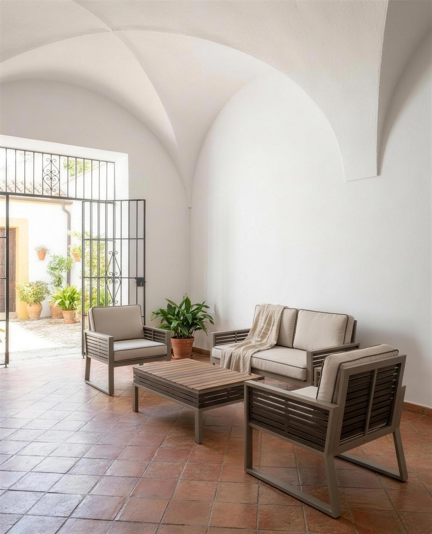 Sofa y sillones Diva bicolor en un zaguan abovedado de suelo de barro, con la reja abierta al patio