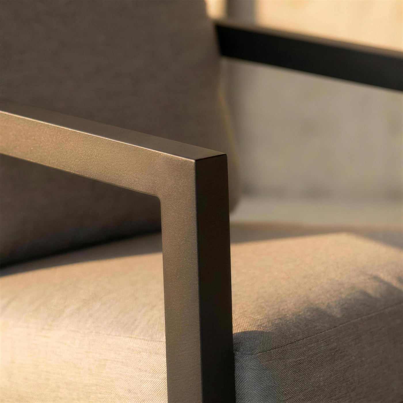 Detalle del brazo de marco abierto de aluminio antracita del sillon Acapulco junto al canto del cojin gris